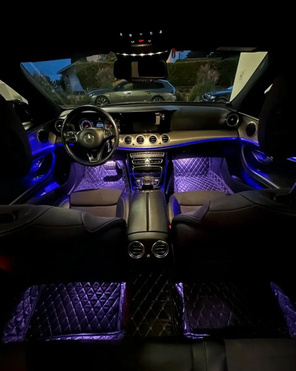 Luxury car interior at night with illuminated purple lighting, leather seats, dashboard, and steering wheel.