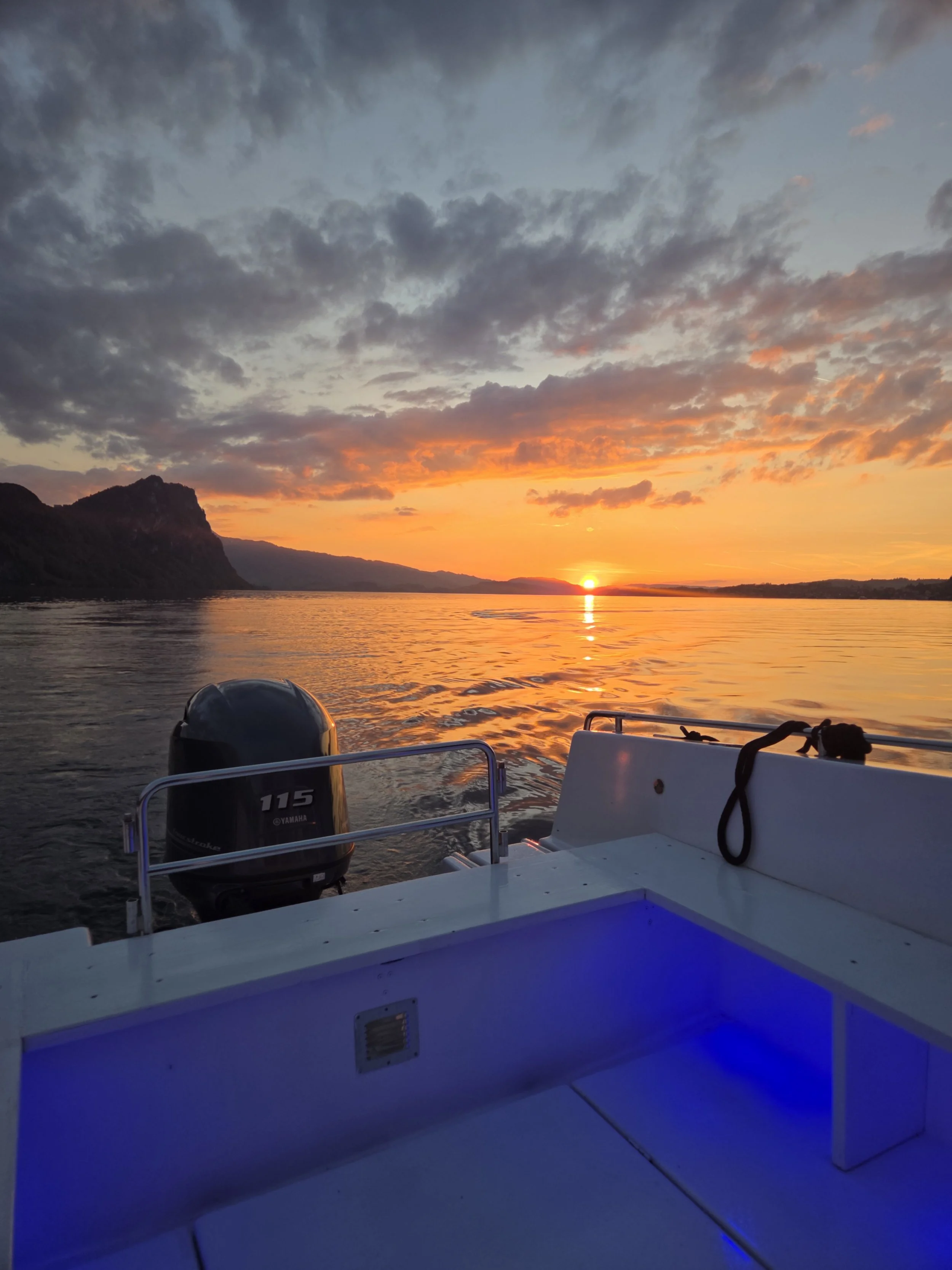 Sunset over a body of water viewed from a boat with a Yamaha outboard motor and a blue-lit seating area.
