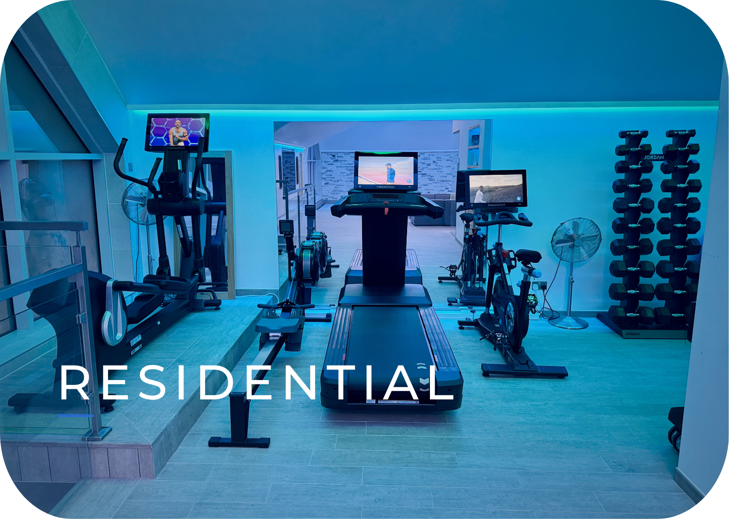 Home gym with treadmill, stationary bikes, elliptical, weight rack, and large monitors, illuminated with blue lighting.