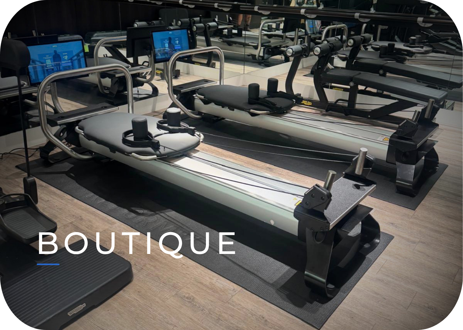 Two rowing machines in a fitness studio with a mirror behind them and screens on the wall.