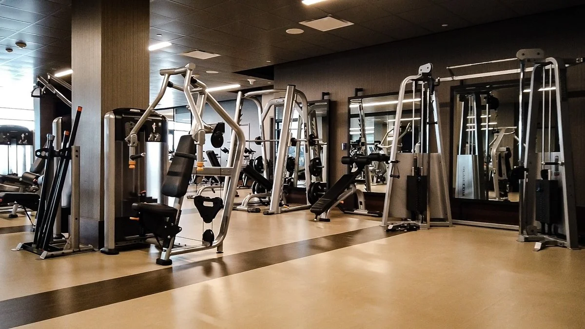 Empty gym with various exercise equipment including weight machines, benches, and mirrors on the wall.