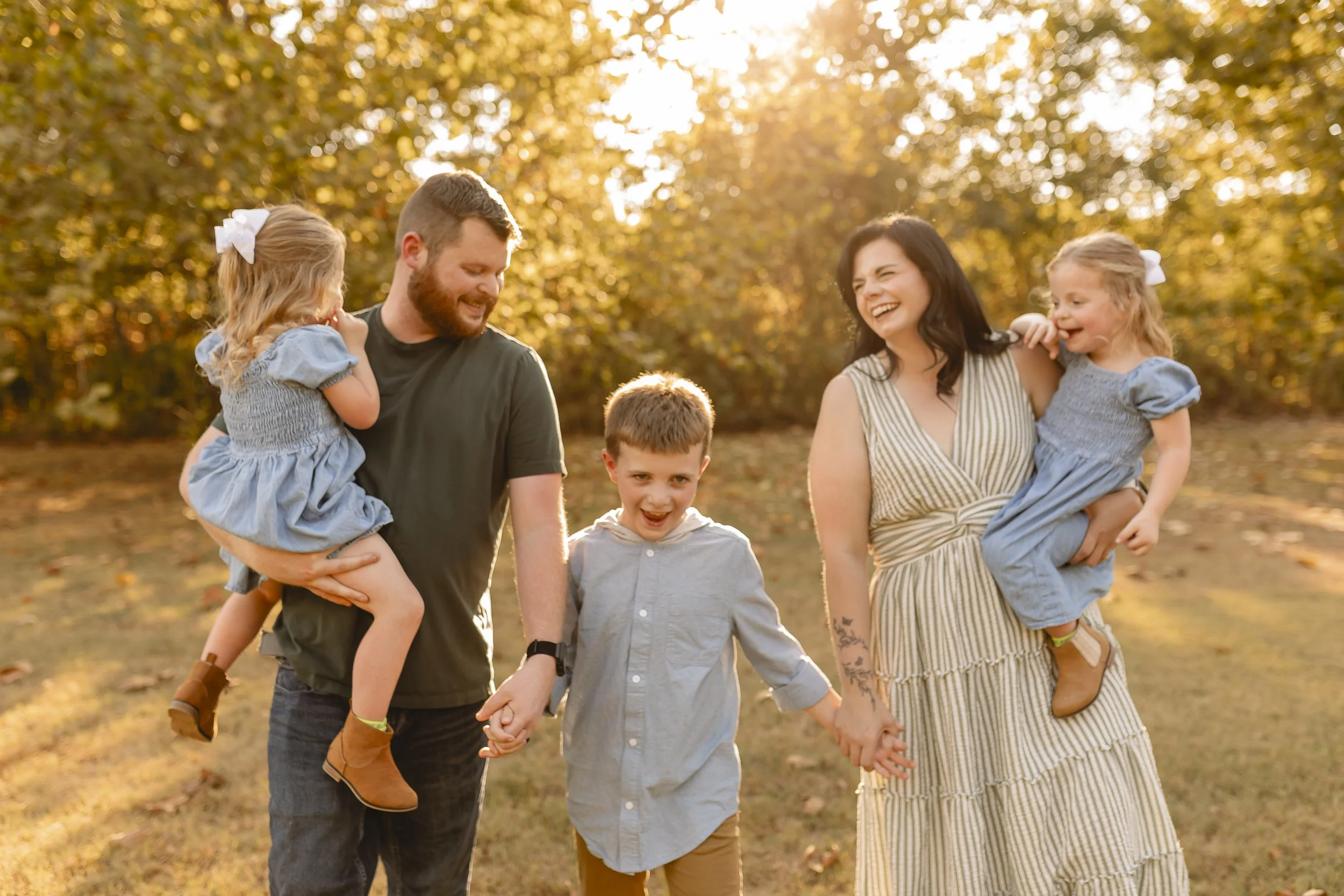 A happy family of six, including two adults and four children, enjoying a walk in a park during autumn, holding hands, and smiling.