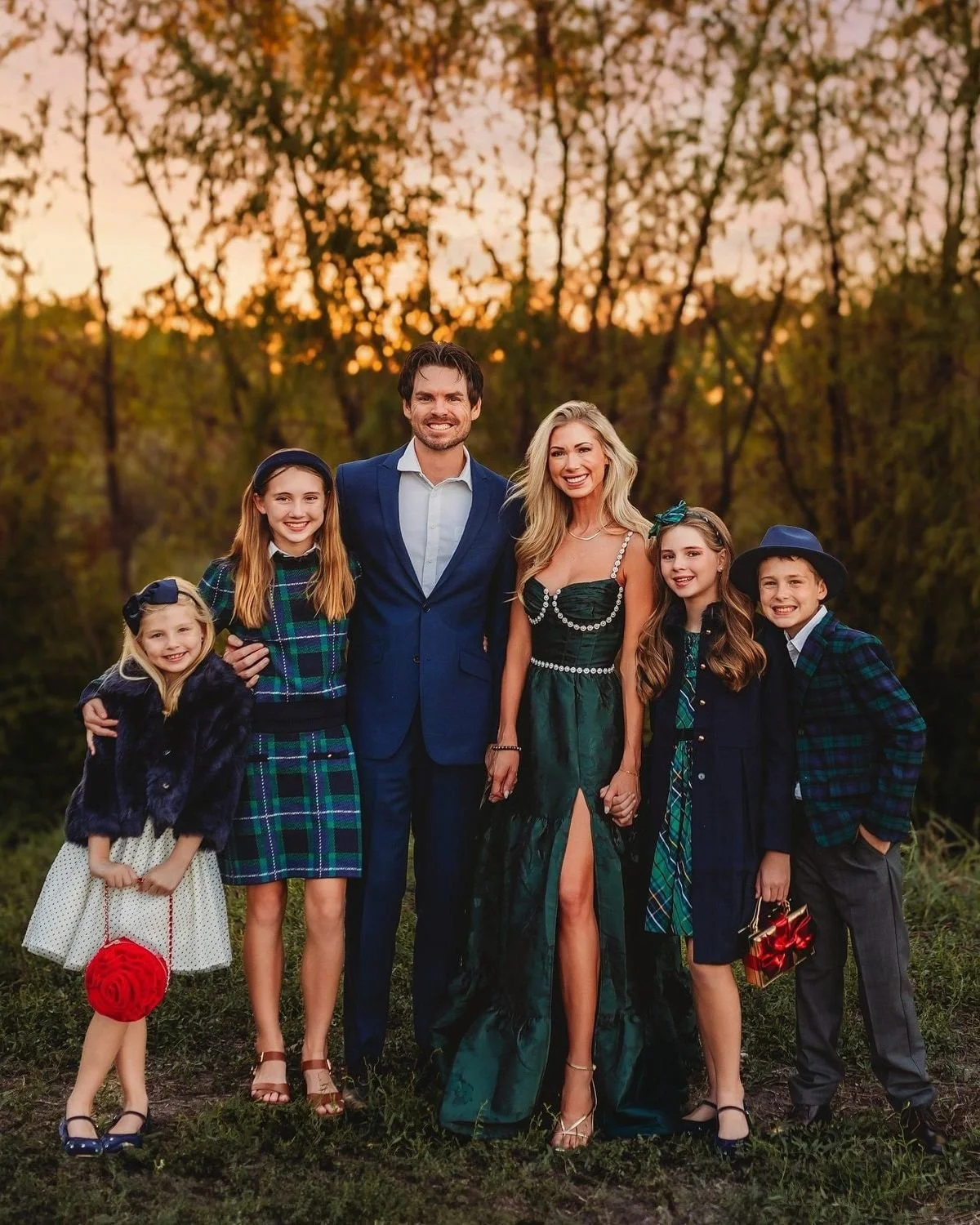 Family of six posing outdoors at sunset, dressed in formal and semi-formal attire with trees in the background.