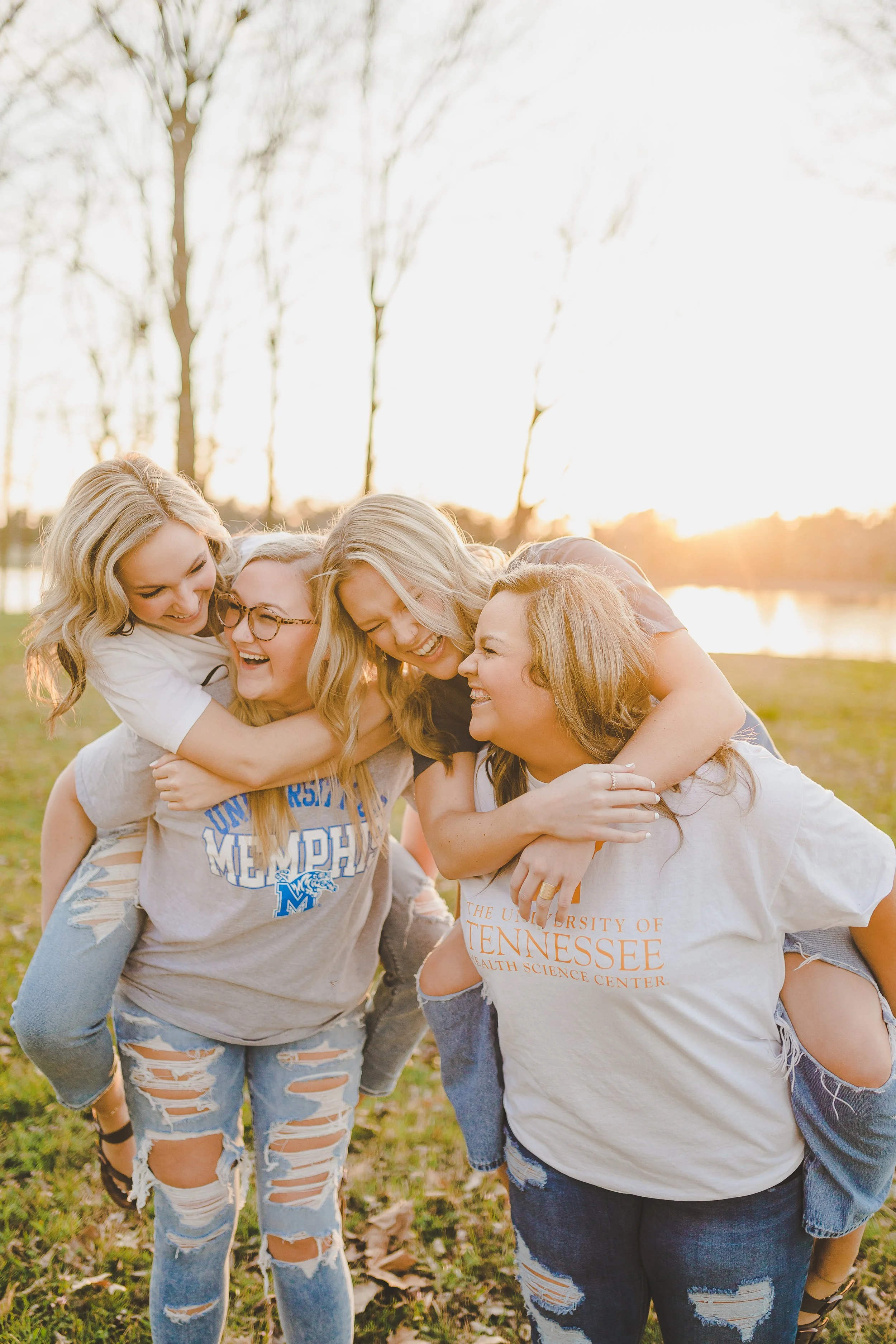 Group of women and girl embracing and smiling outdoors during sunset, wearing casual clothes and jeans.