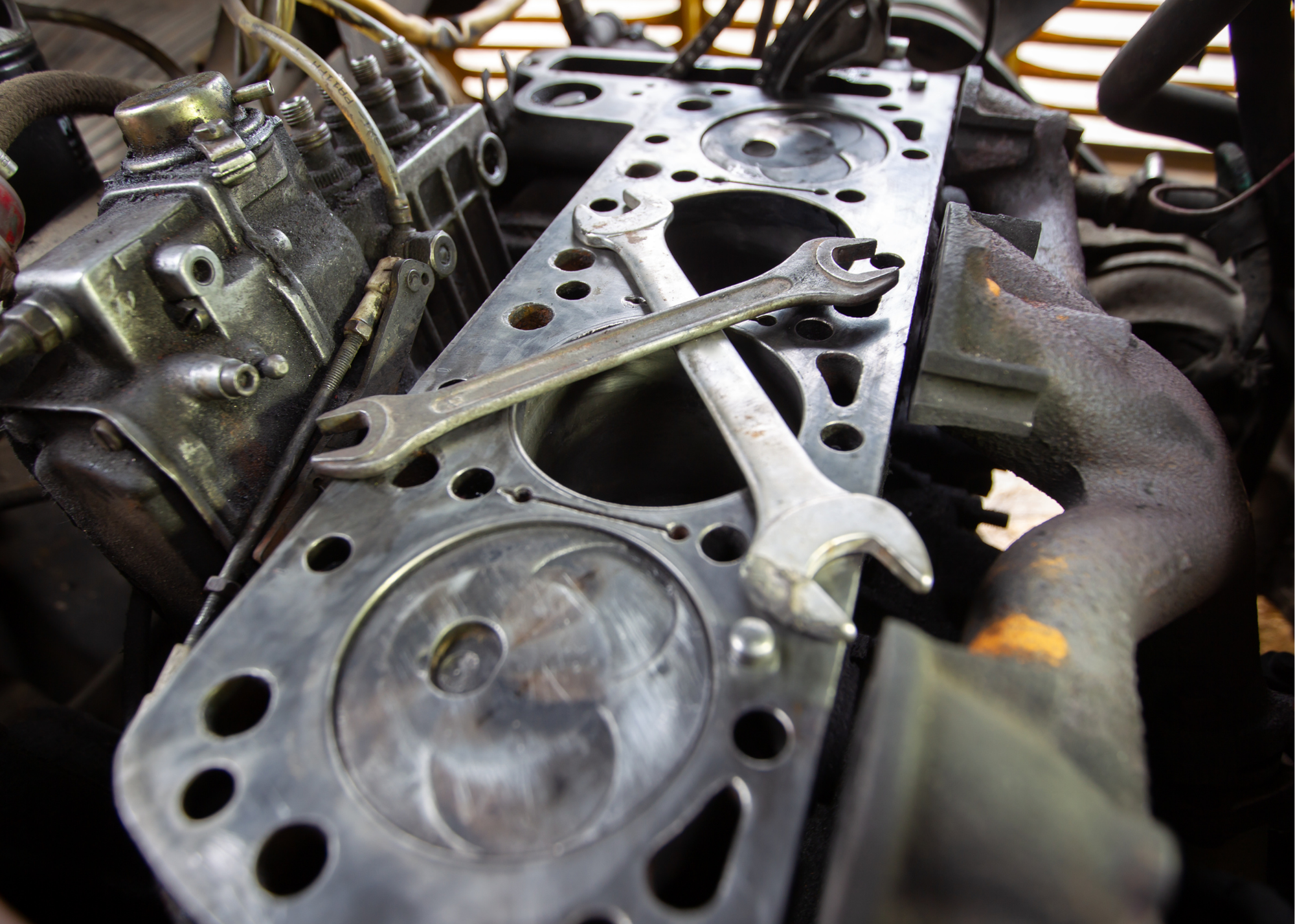 Close-up of an old, disassembled car engine with visible cylinder head and wrenches placed on top.