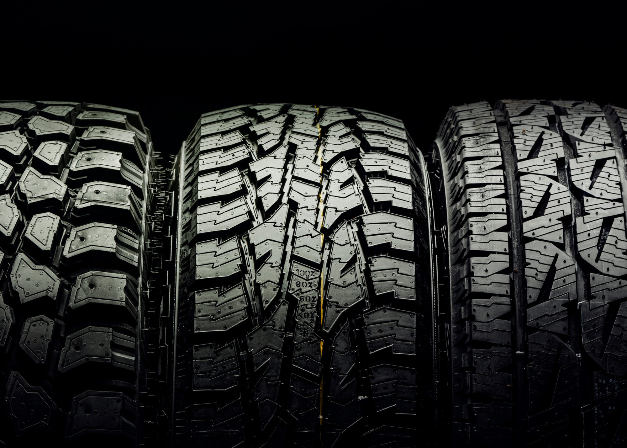 Three tires with different tread patterns are lined up side by side against a black background.