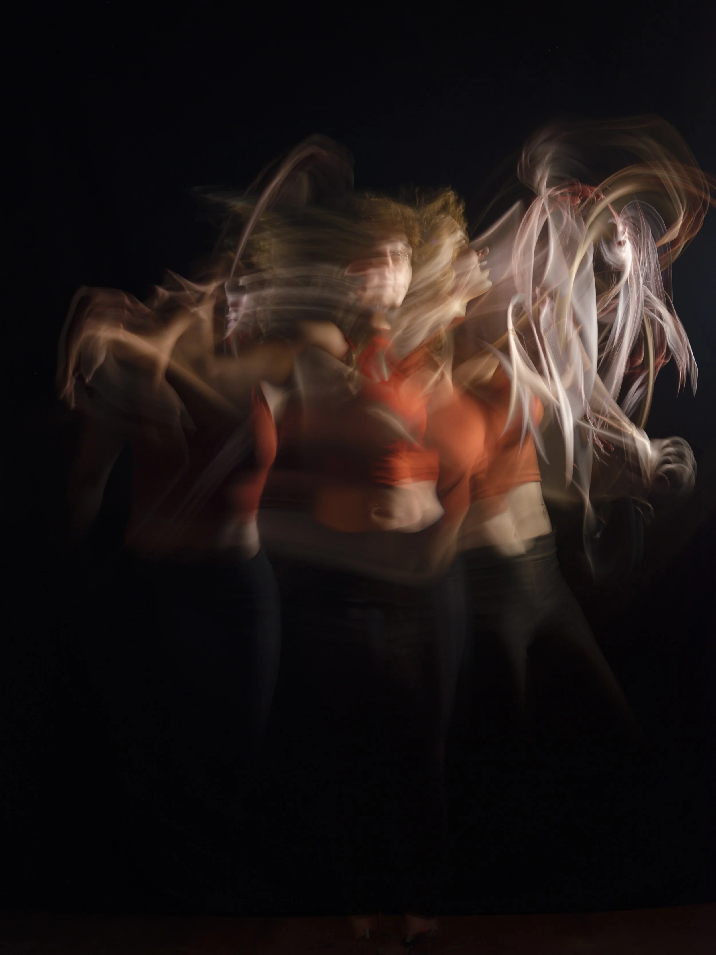 Blurred image of a group of people dancing or moving quickly against a dark background, creating a streaking effect with motion.