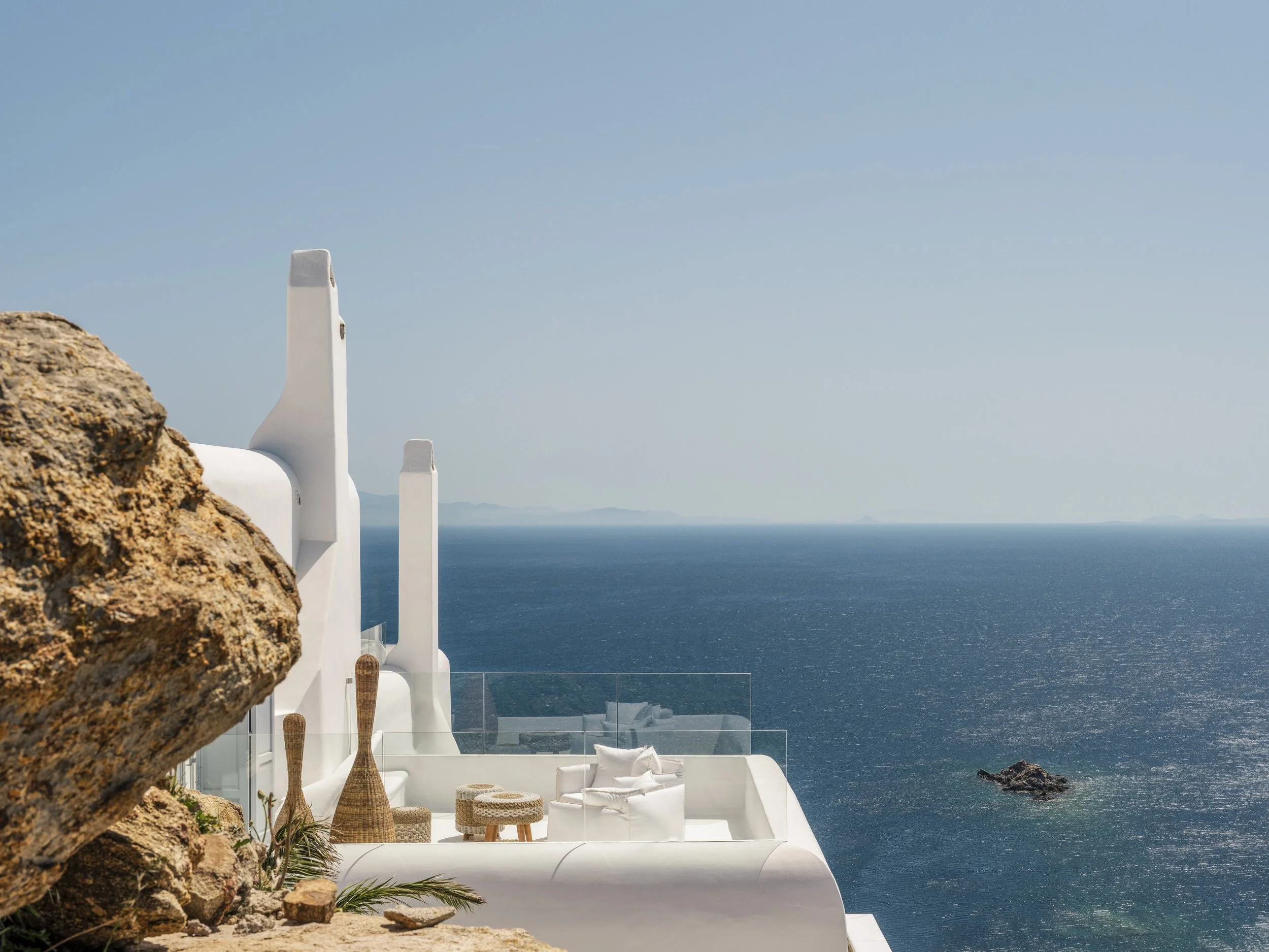 White modern building with smooth curves and outdoor seating overlooking the ocean under a clear sky.