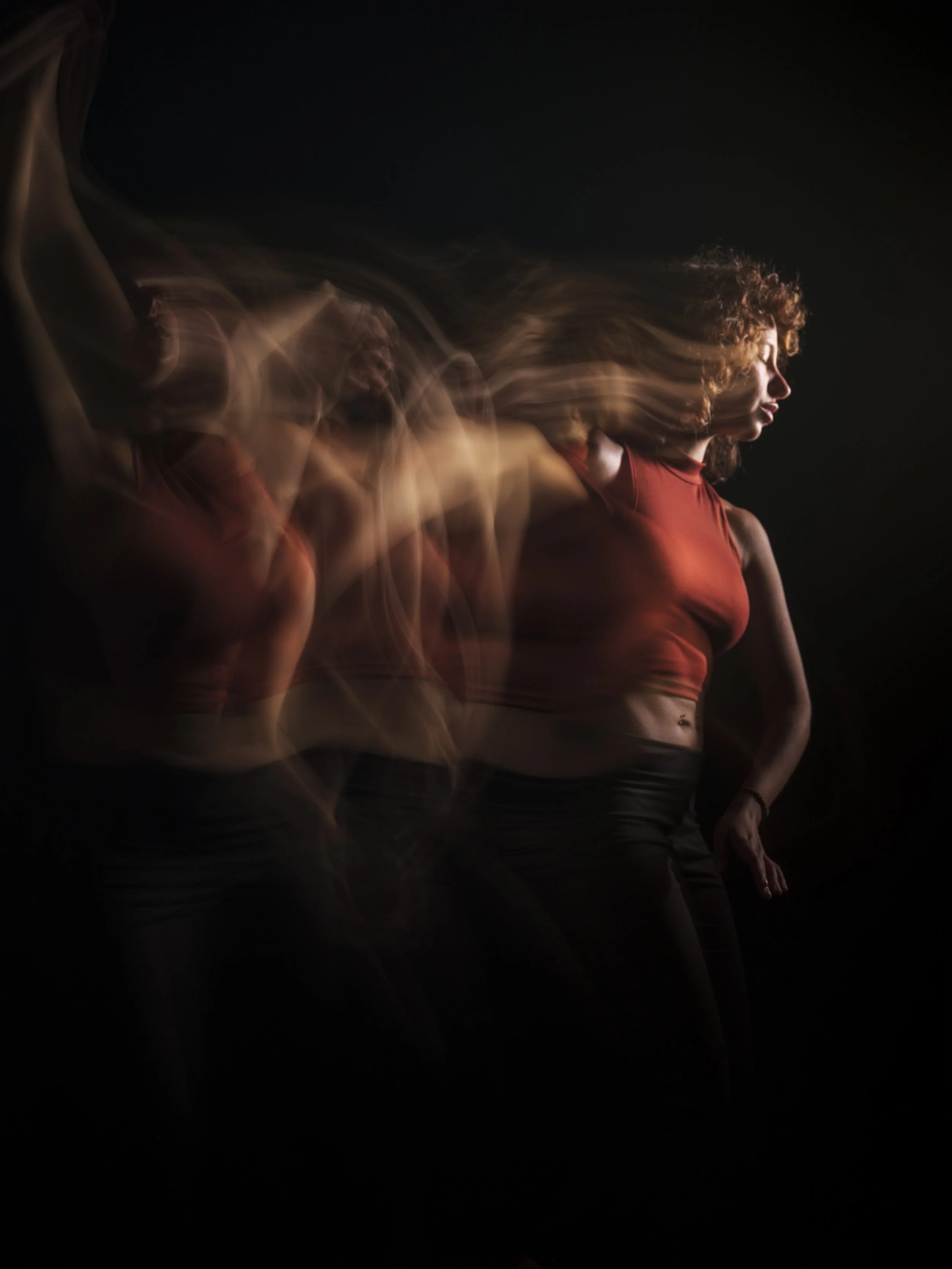 A woman in a red sleeveless top is photographed against a black background. Her hair and face appear to be moving, creating a ghostly, blurred effect.