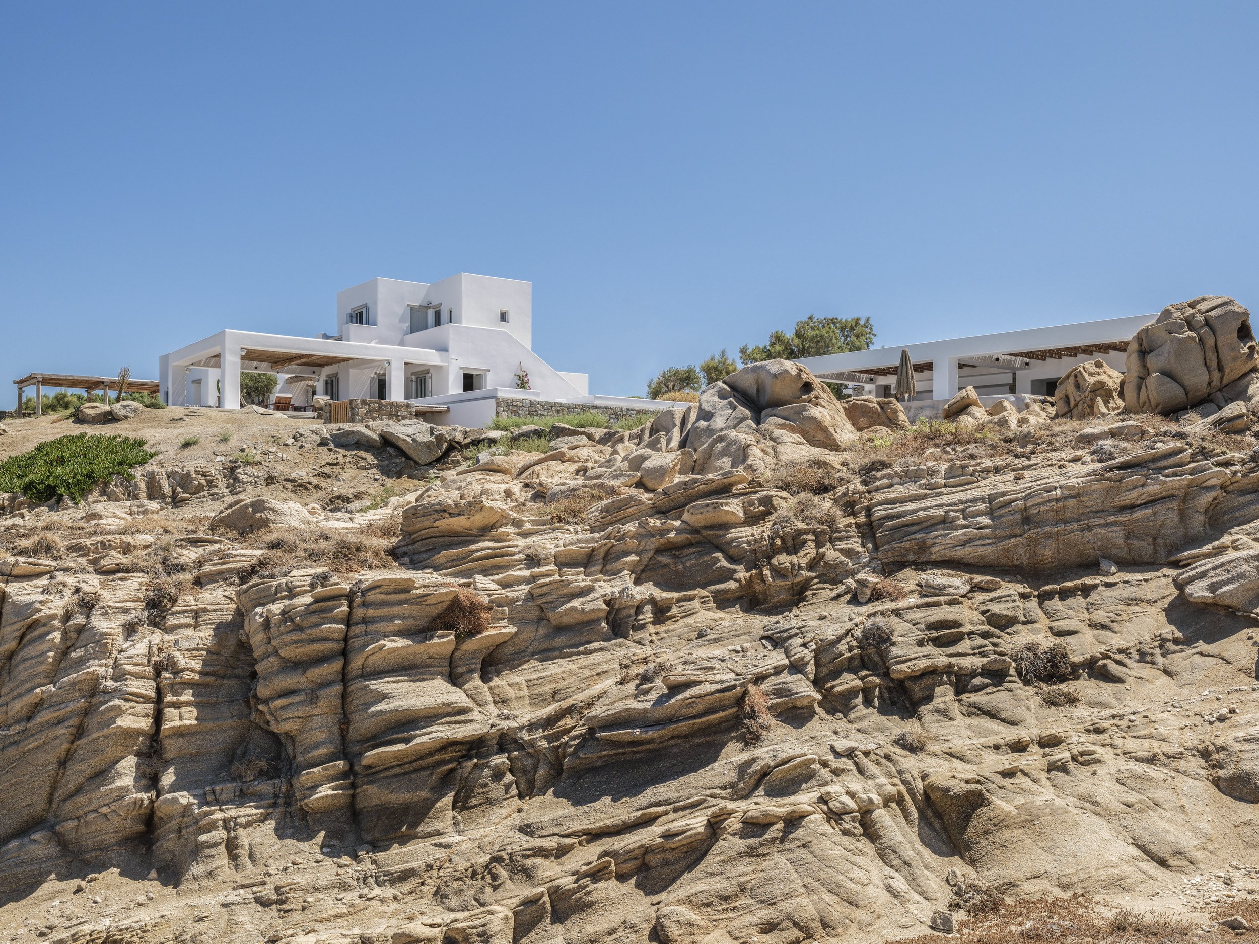 A white modern house on a rocky hill under a clear blue sky.