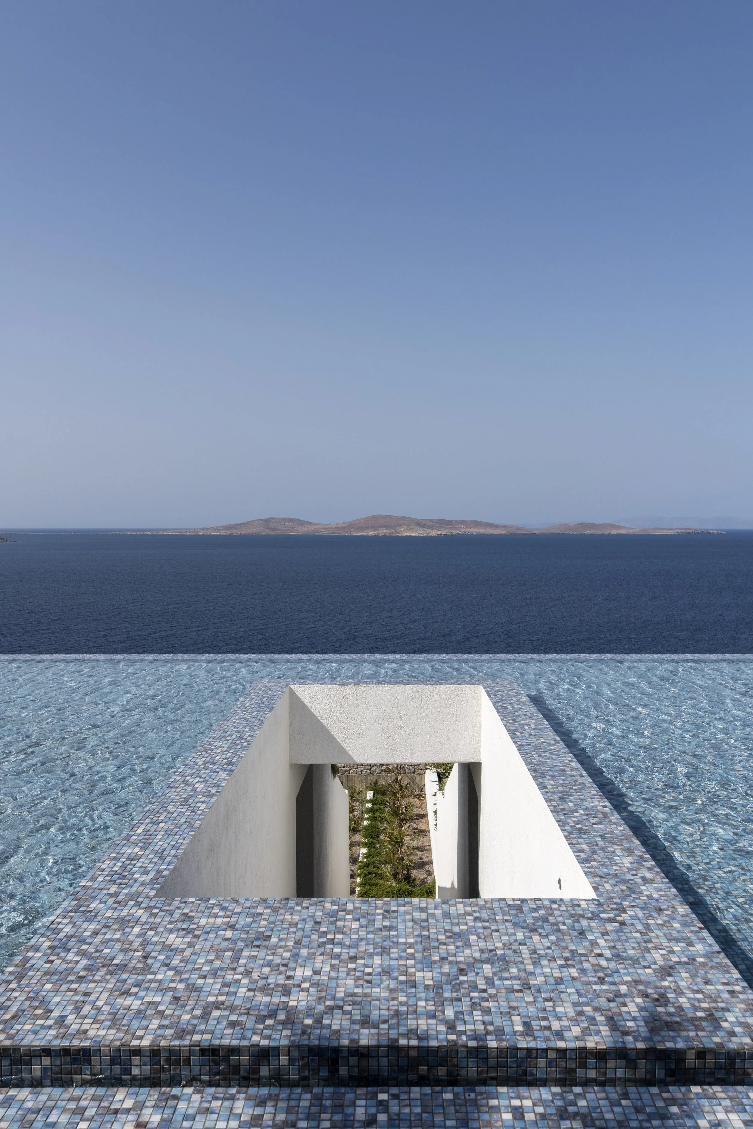 Infinity pool with mosaic tile edge overlooking the Aegean sea and distant islands under a clear blue sky located in Mykonos island Greece