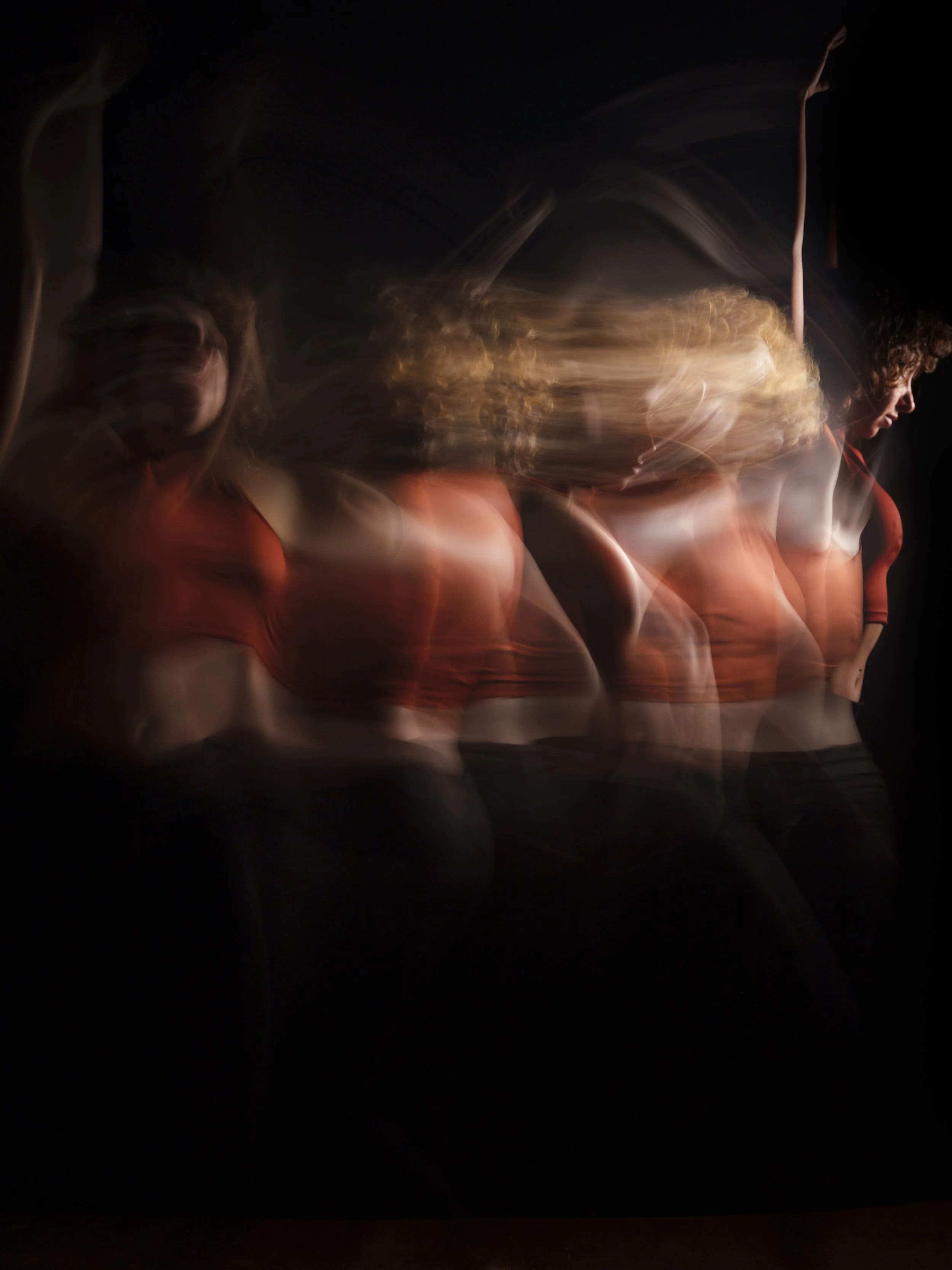A dancer captures multiple blurred images in motion, wearing an orange outfit, creating a layered effect against a black background.