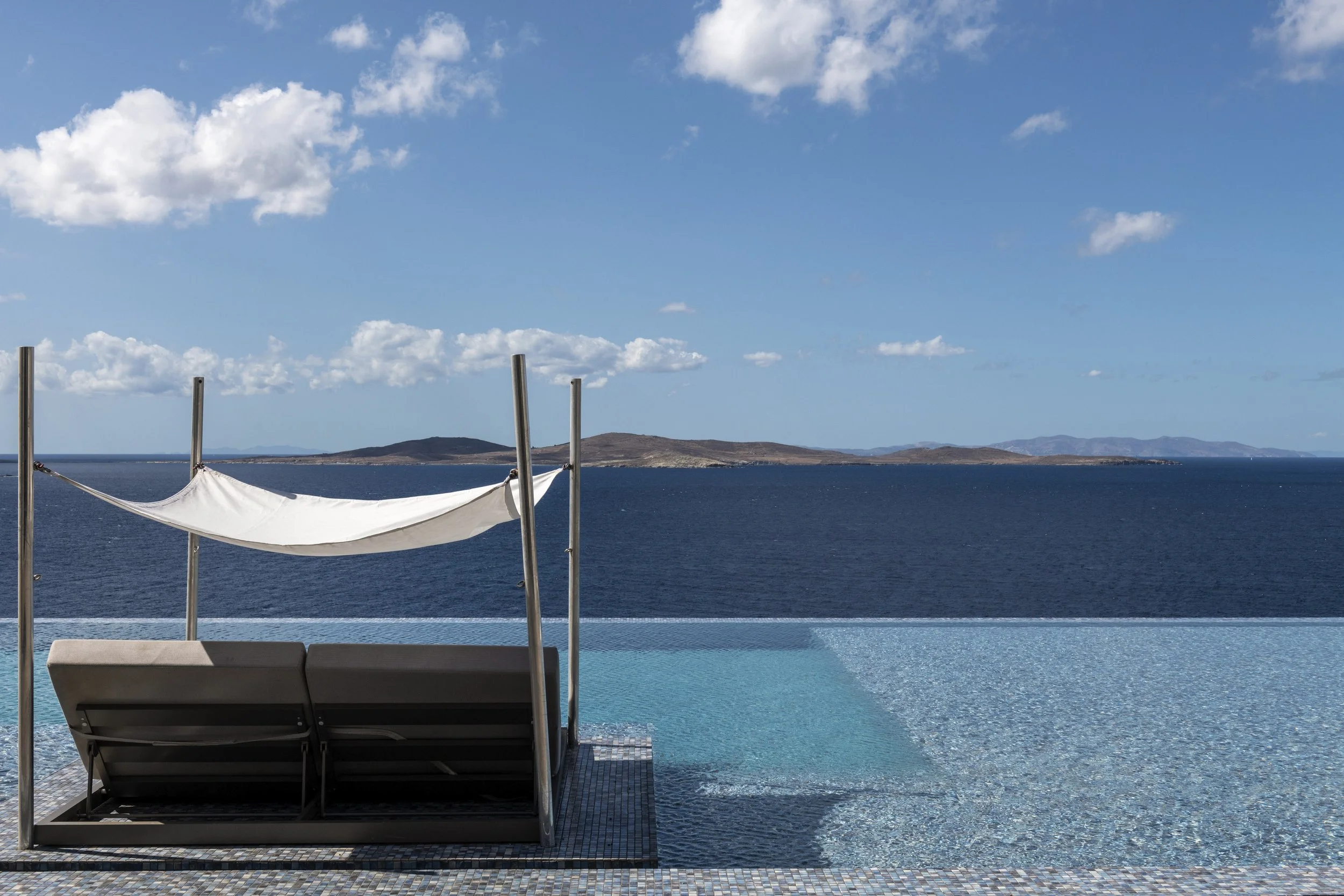 Infinity pool with mosaic tile edge overlooking the Aegean sea and distant islands under a clear blue sky located in Mykonos island Greece