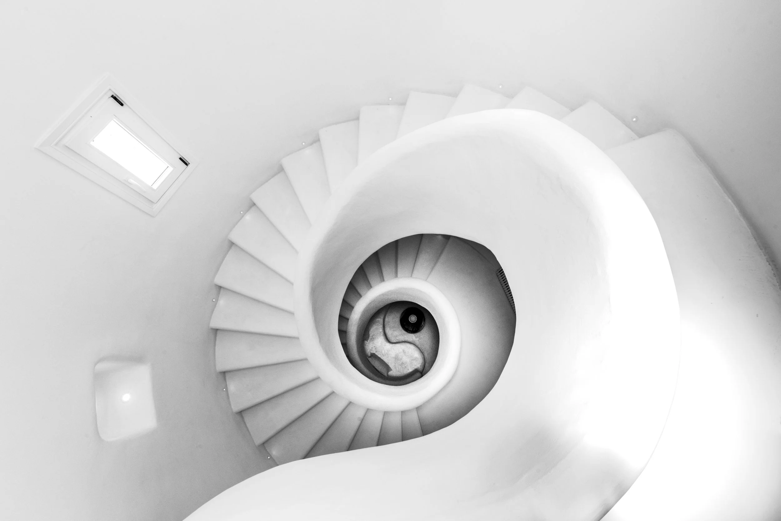 Black and white photo looking down a spiral staircase with a small window at the top