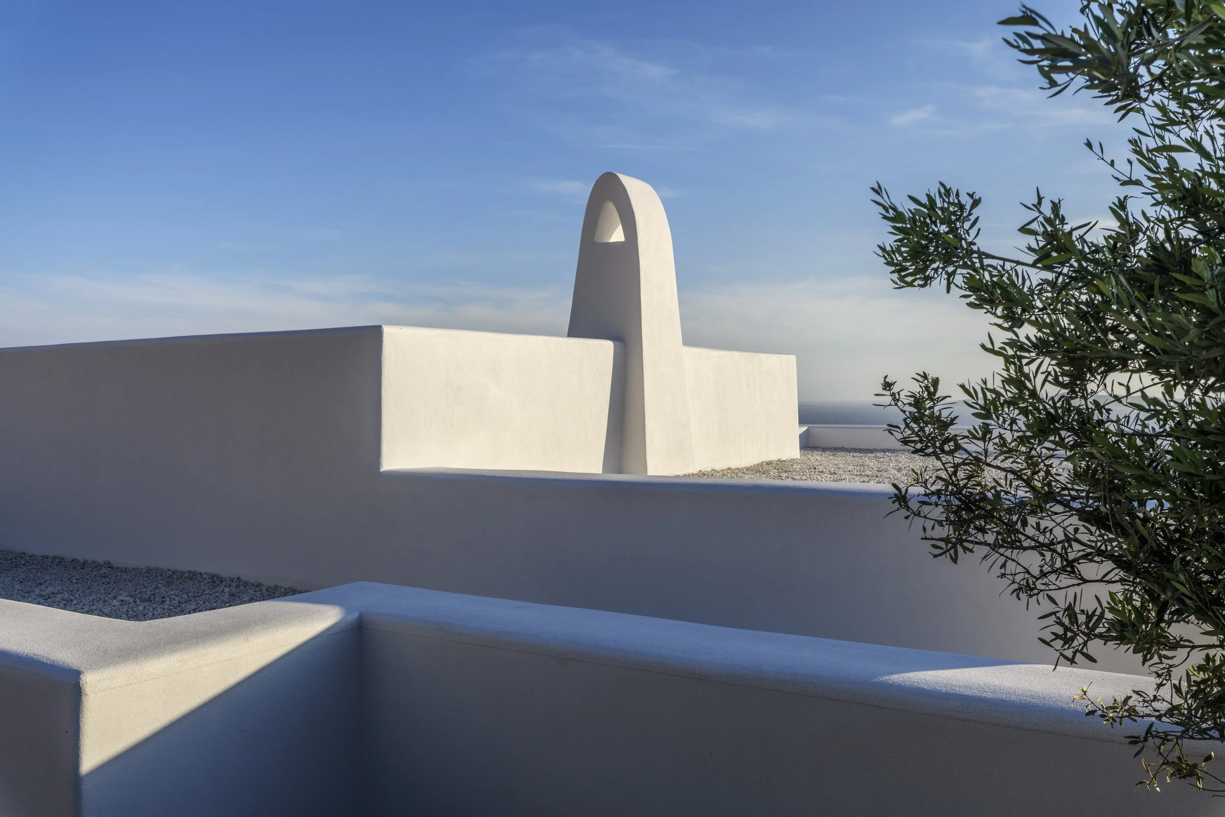 Elegant architectural shot of a luxury Mykonos island property featuring stark white stucco walls and a traditional sculptural chimney against a vibrant blue sky.