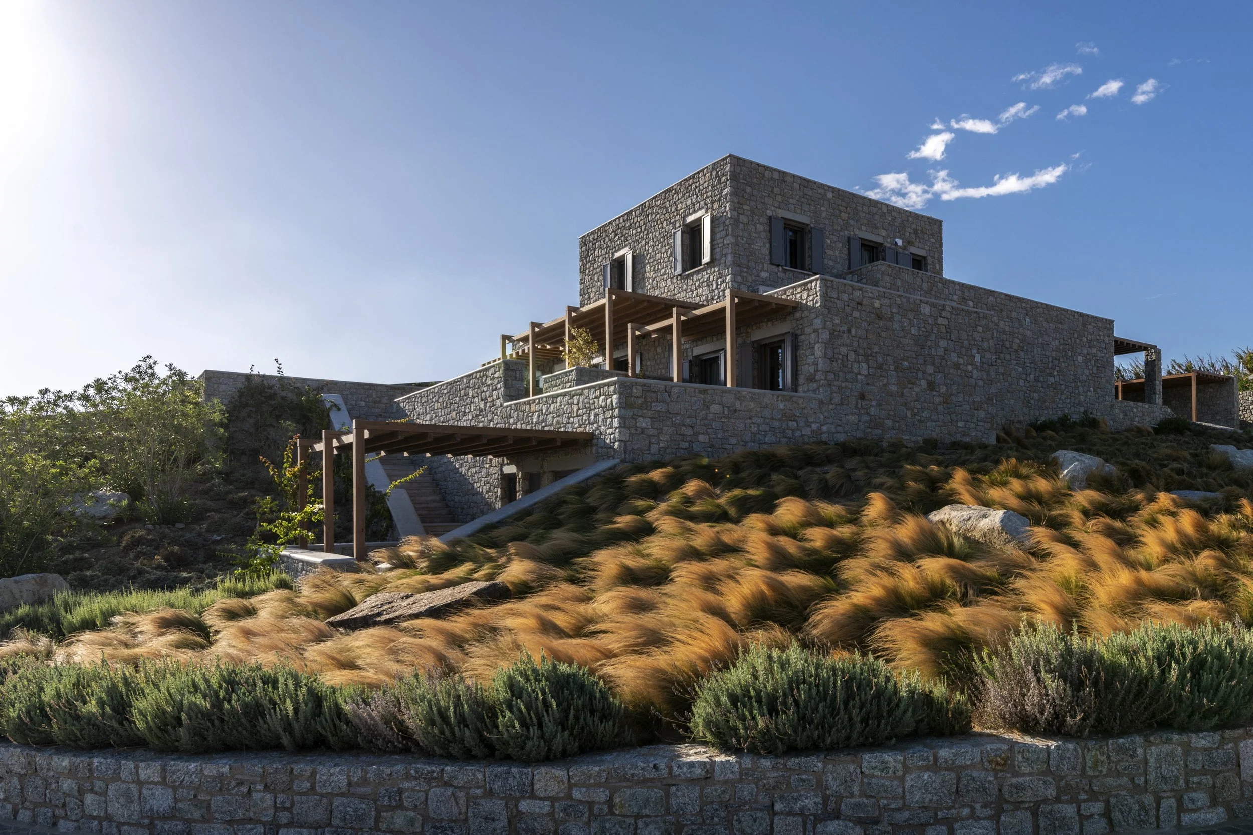 A modern stone building on a hill with surrounded by desert plants and a clear blue sky.