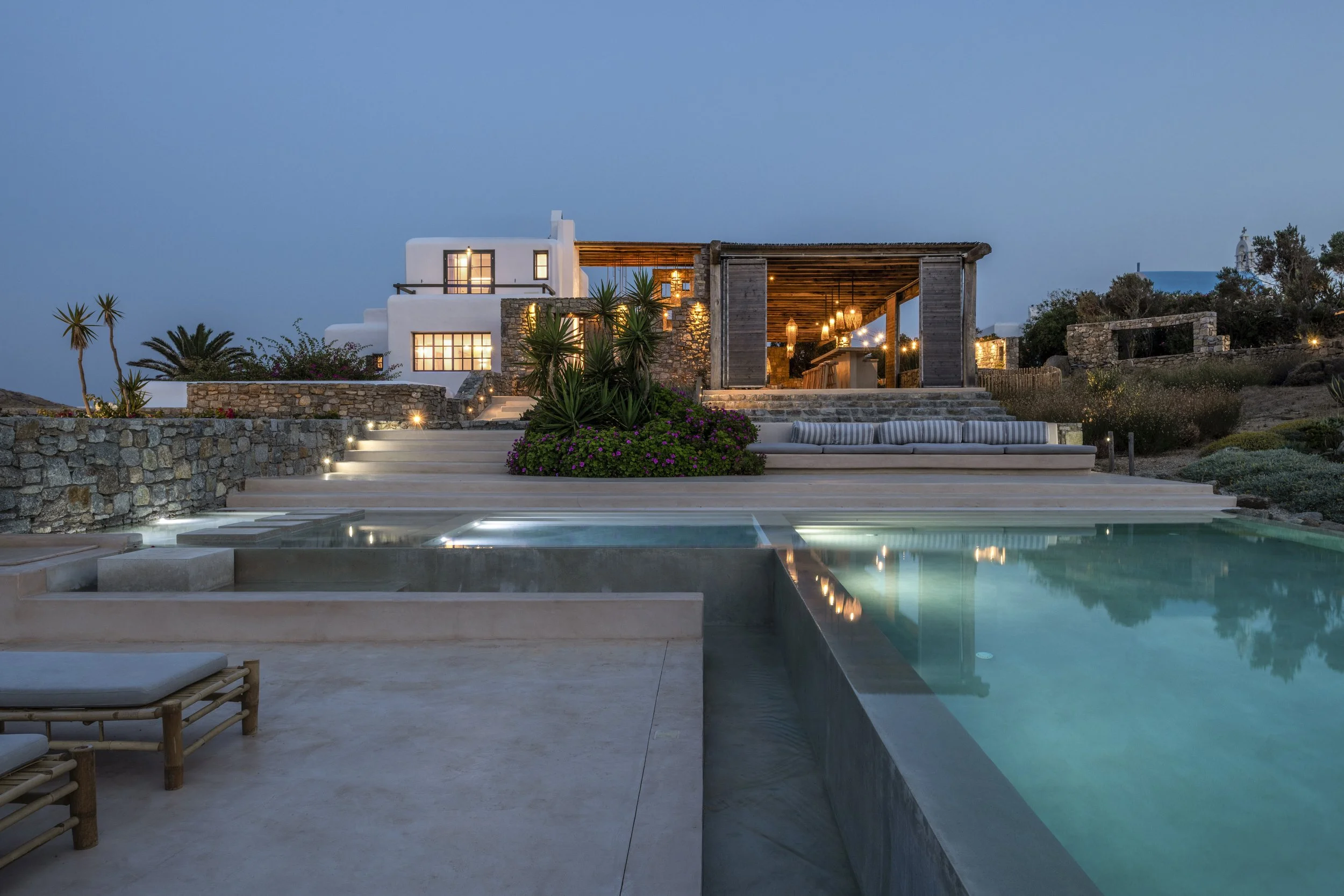 Luxury house with a swimming pool, outdoor lounge area, and ambient lighting, set against a twilight sky.