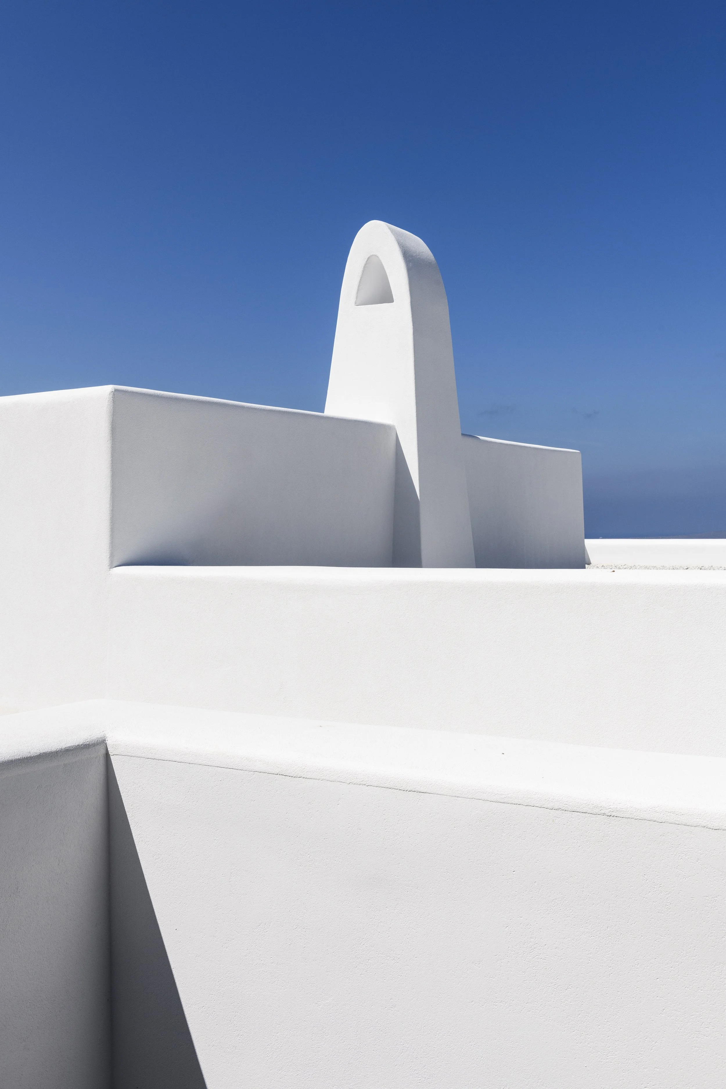 White modern building with smooth curves and arch-shaped windows against a clear blue sky.