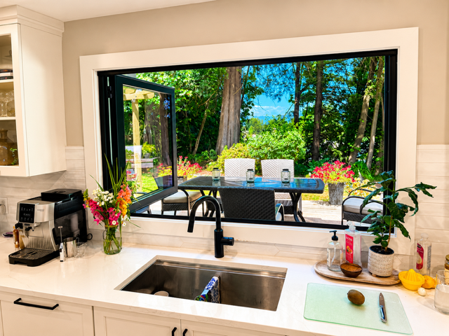 Black aluminum folding kitchen window open to a garden patio