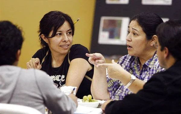 Three people engaged in a discussion around a table, with a woman gesturing with her hands.