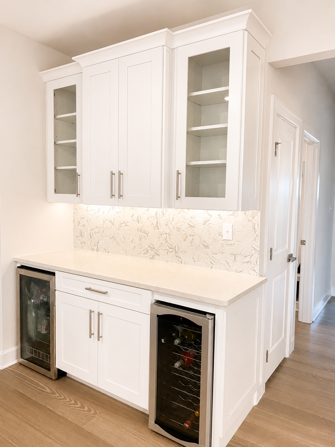 Modern kitchen bar area with white cabinetry, marble backsplash, and built-in wine coolers.