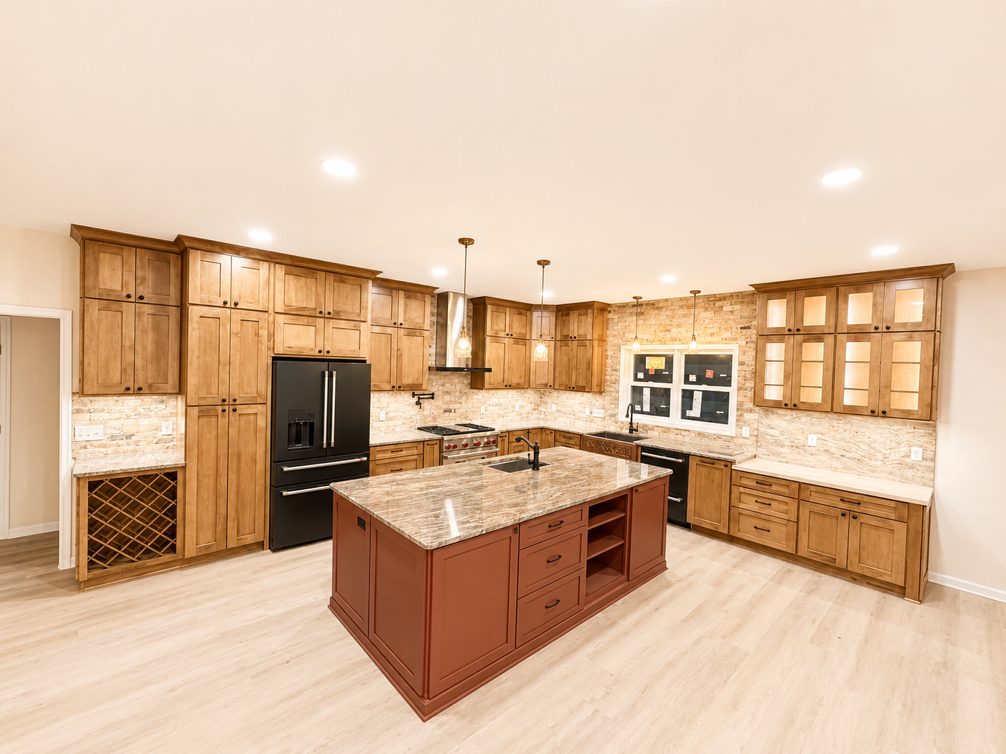Bright kitchen with wooden cabinets, black appliances, and a central island with a granite countertop. Recessed ceiling lights, brick backsplash, and a window above the sink.