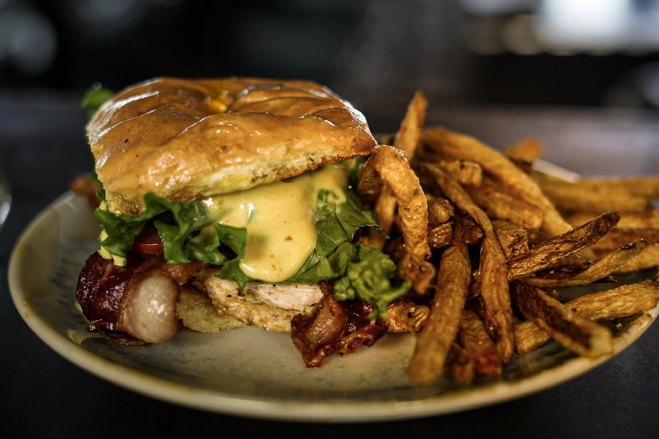 A bowl containing a sandwich with lettuce, tomato, cheese, bacon, and a toasted bun, along with a side of crispy French fries.