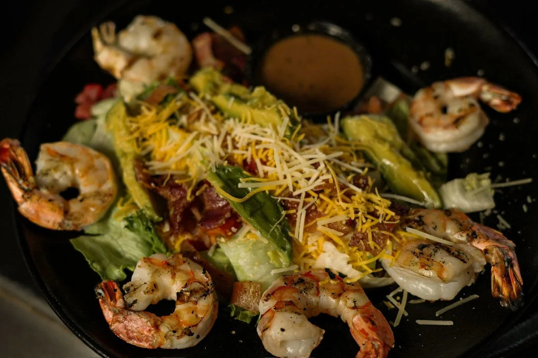 Shrimp on a bed of lettuce topped with shredded cheese and grilled vegetables in a black skillet
