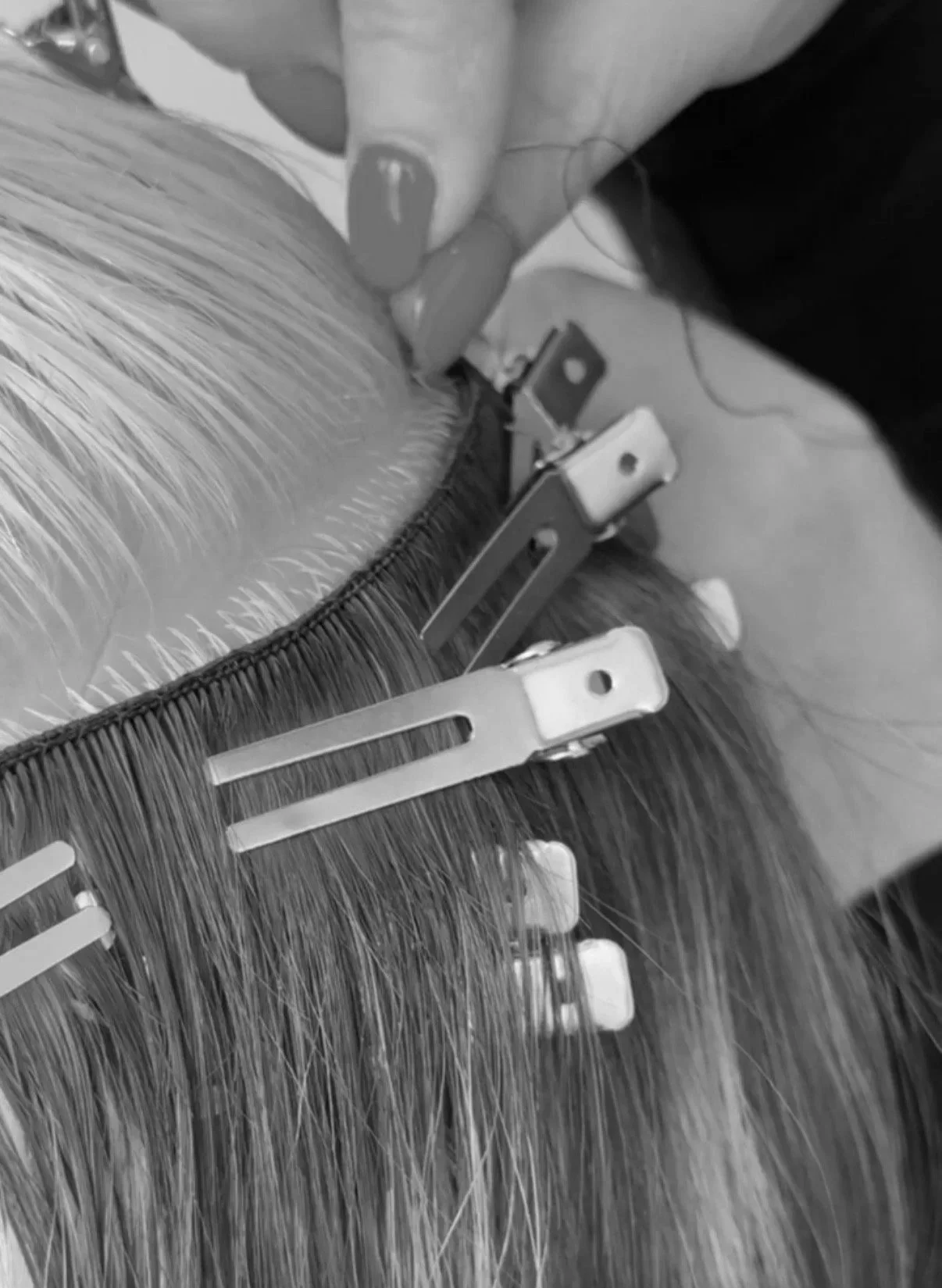Close-up of a person's hand pinning hair extensions to natural hair with metal clips.