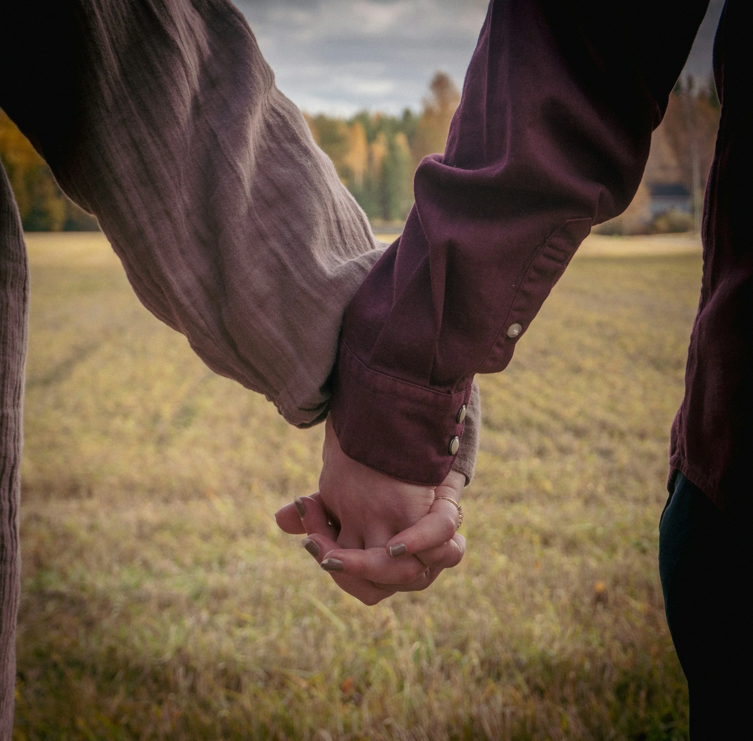 Two people holding hands outdoors in a natural setting during autumn.