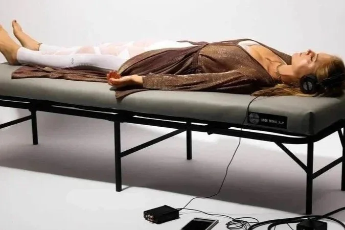A woman lying on a medical examination table, wearing headphones, with her eyes closed in a relaxed pose.