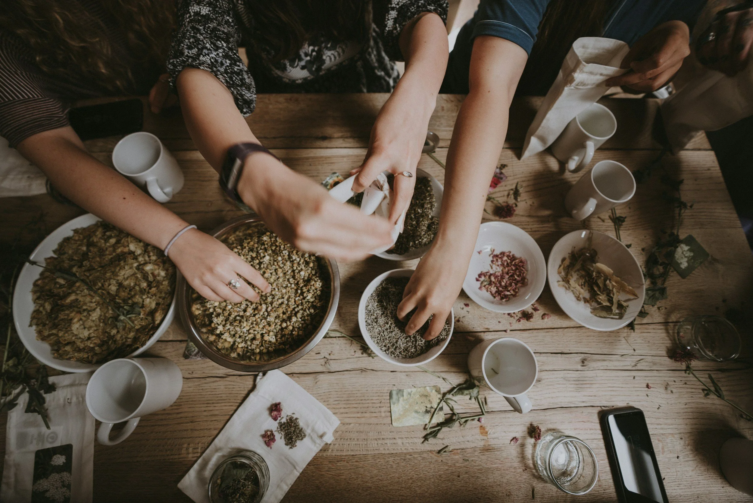 People gathered around a wooden table with various dishes, including salads and snacks, preparing or sharing food.