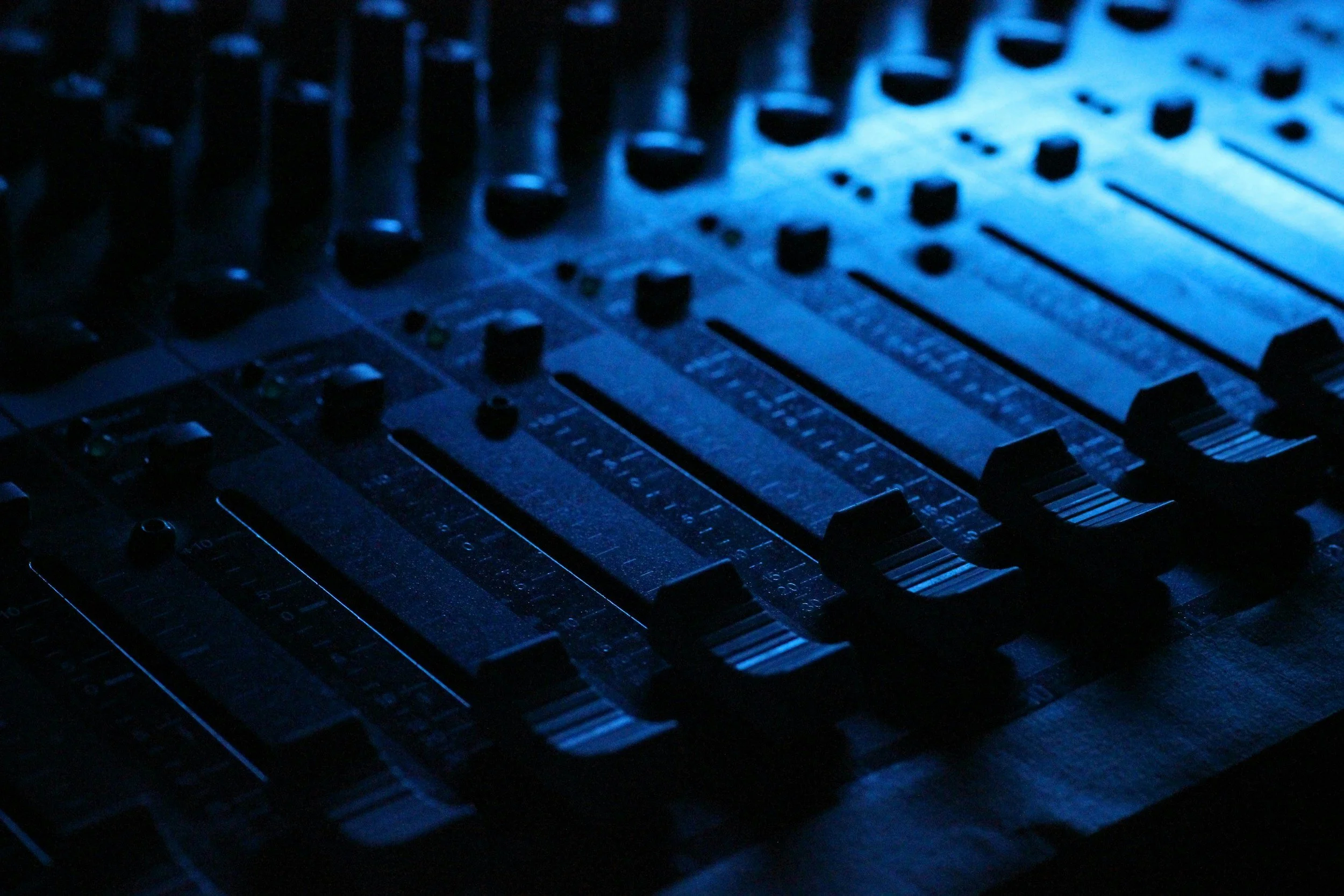 Close-up of a sound mixing console with illuminated faders and knobs in a studio environment, we do music promotions and features.