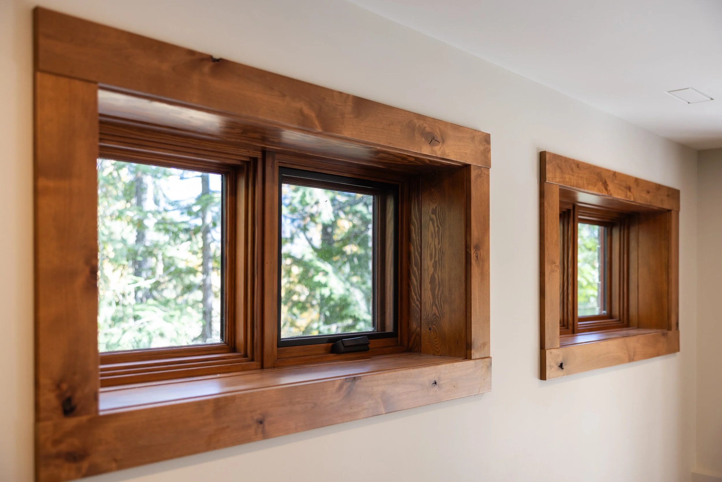 Two wooden framed windows in a house wall, with trees visible outside.