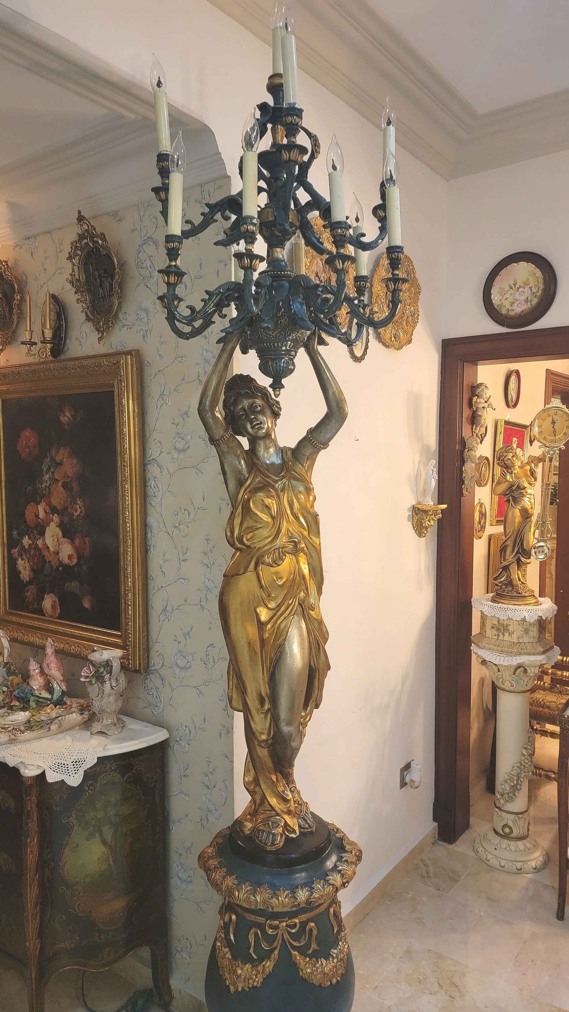 A gold and dark-colored statue of a woman holding a chandelier with candle-shaped light bulbs.