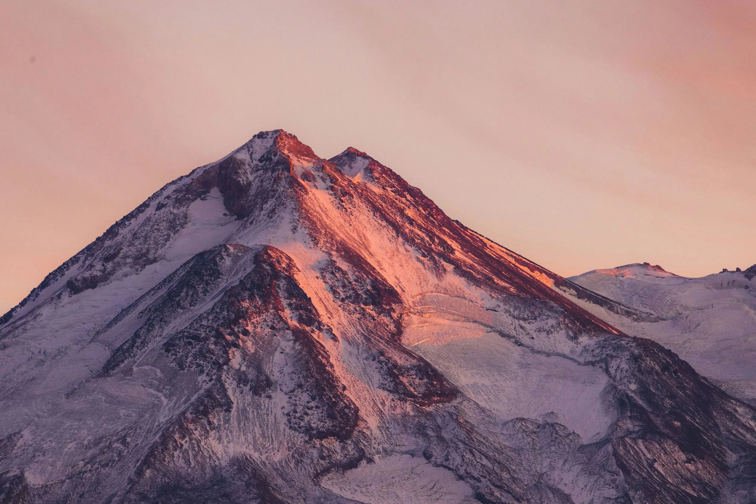 Snow-capped mountain peak during sunset with pink and purple sky.