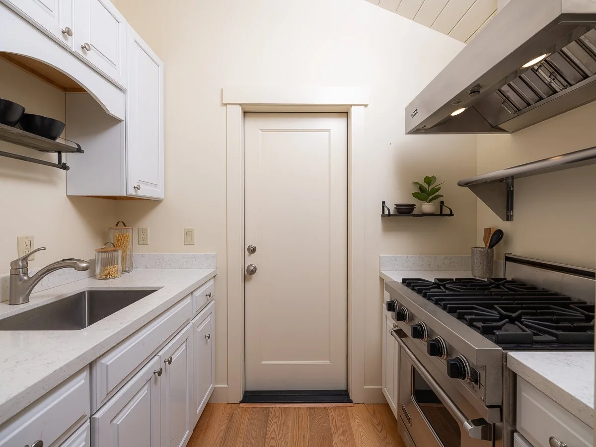 White kitchen with countertop, sink, stove, and a door in the middle.