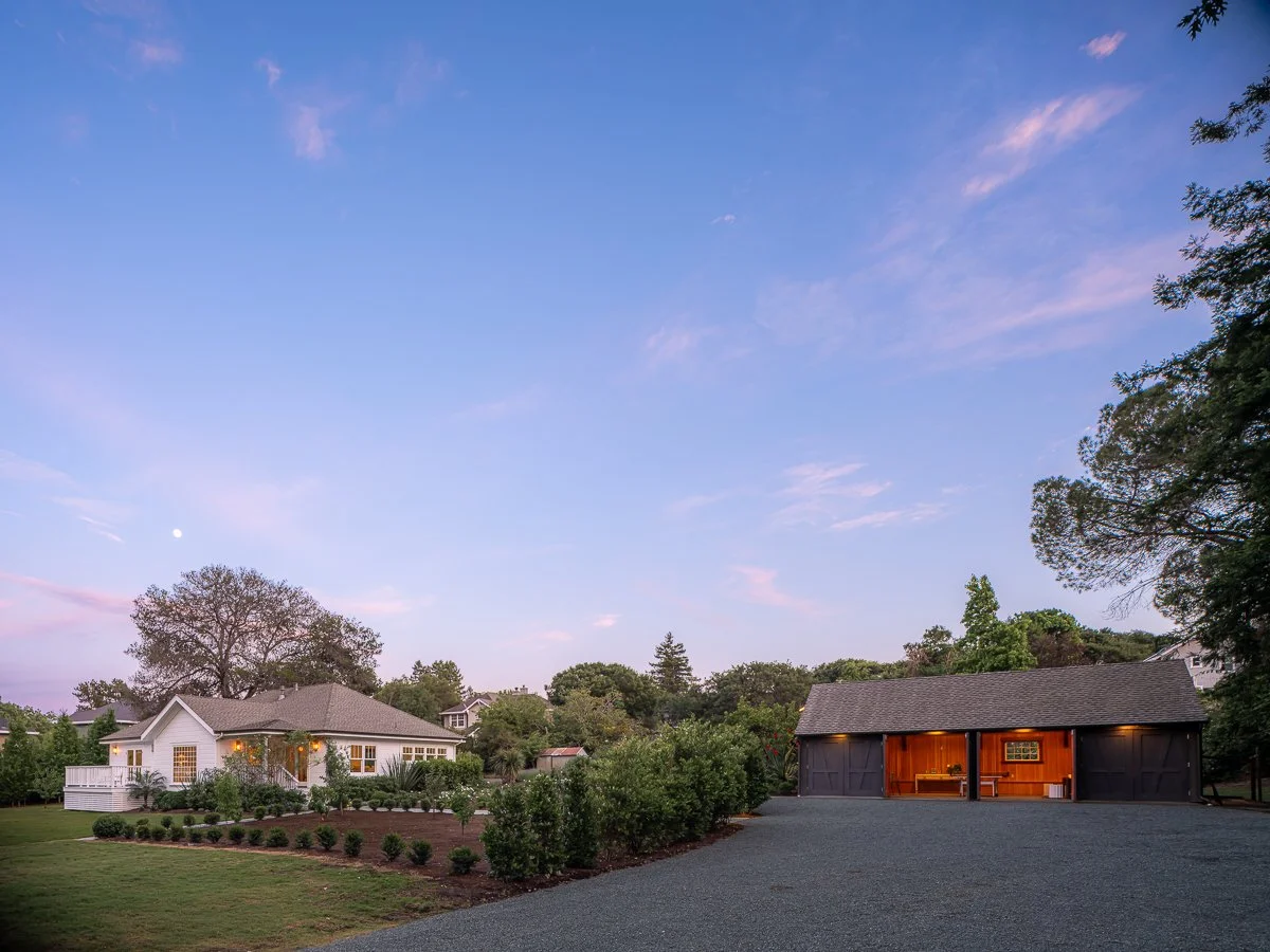 Residential backyard with a white house, garden, and a gray garage with open doors at dusk.