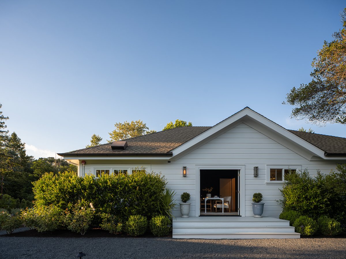 White house with open door, front porch, surrounded by greenery, under a clear blue sky.