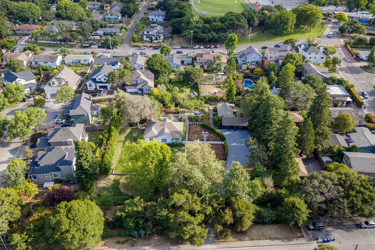 Aerial view of a neighborhood with houses, trees, and a few swimming pools in backyards.