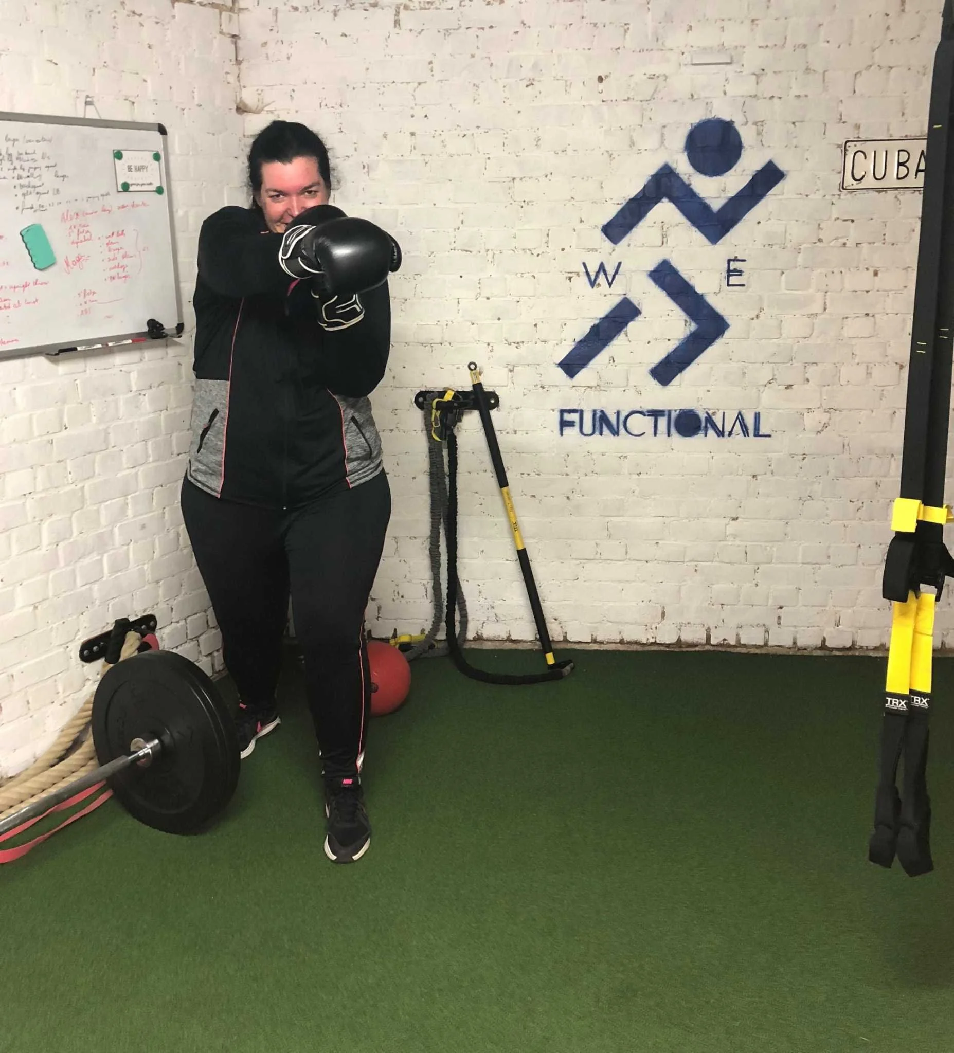 Vrouw met boxinghandschoenen poseert in een sportschool met fitnessuitrusting en een muur met logo van 'W3F'.