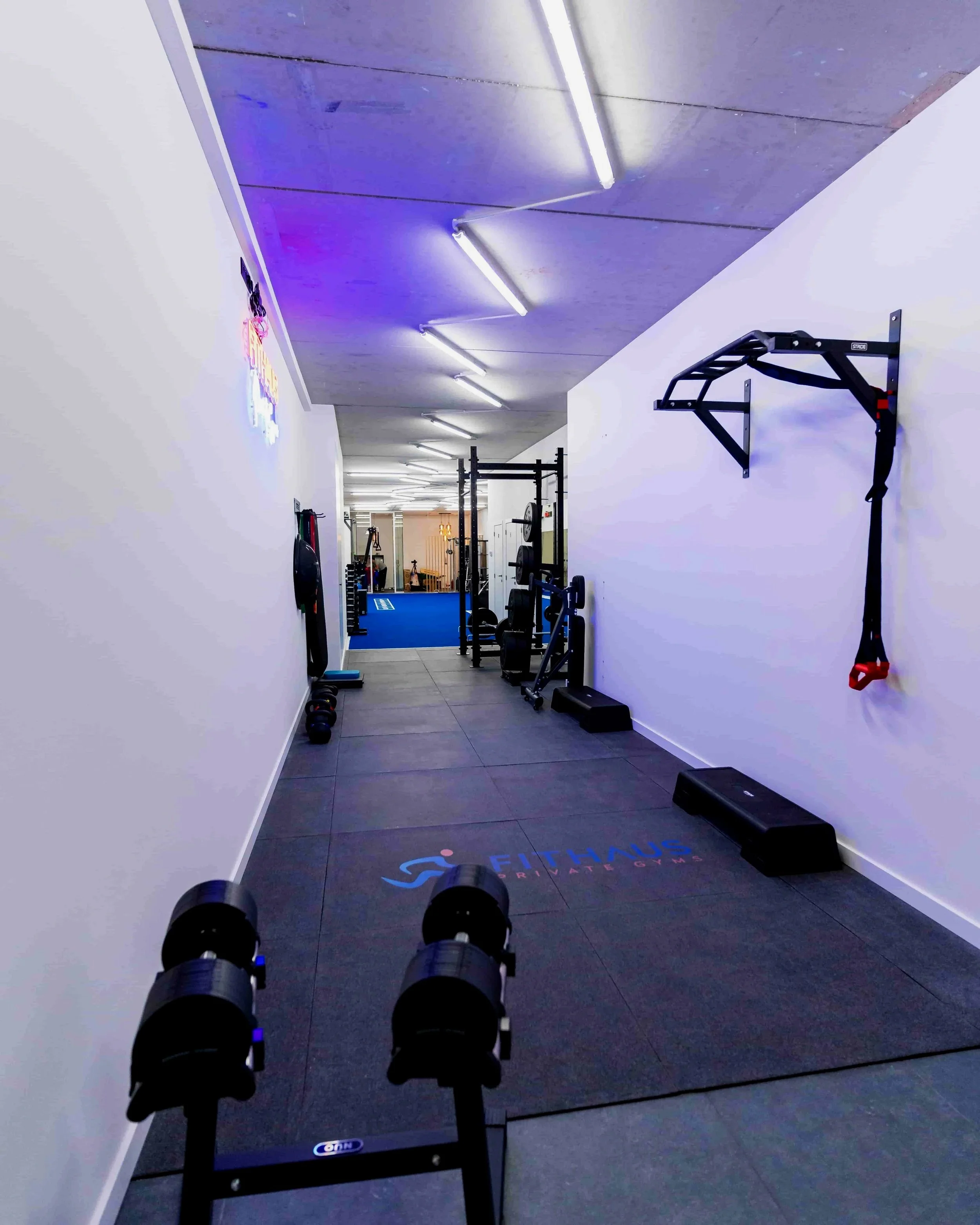 Binnenkant van een sportschool met fitnessapparatuur, gewichten en een mat met het logo 'Fithaul'.
