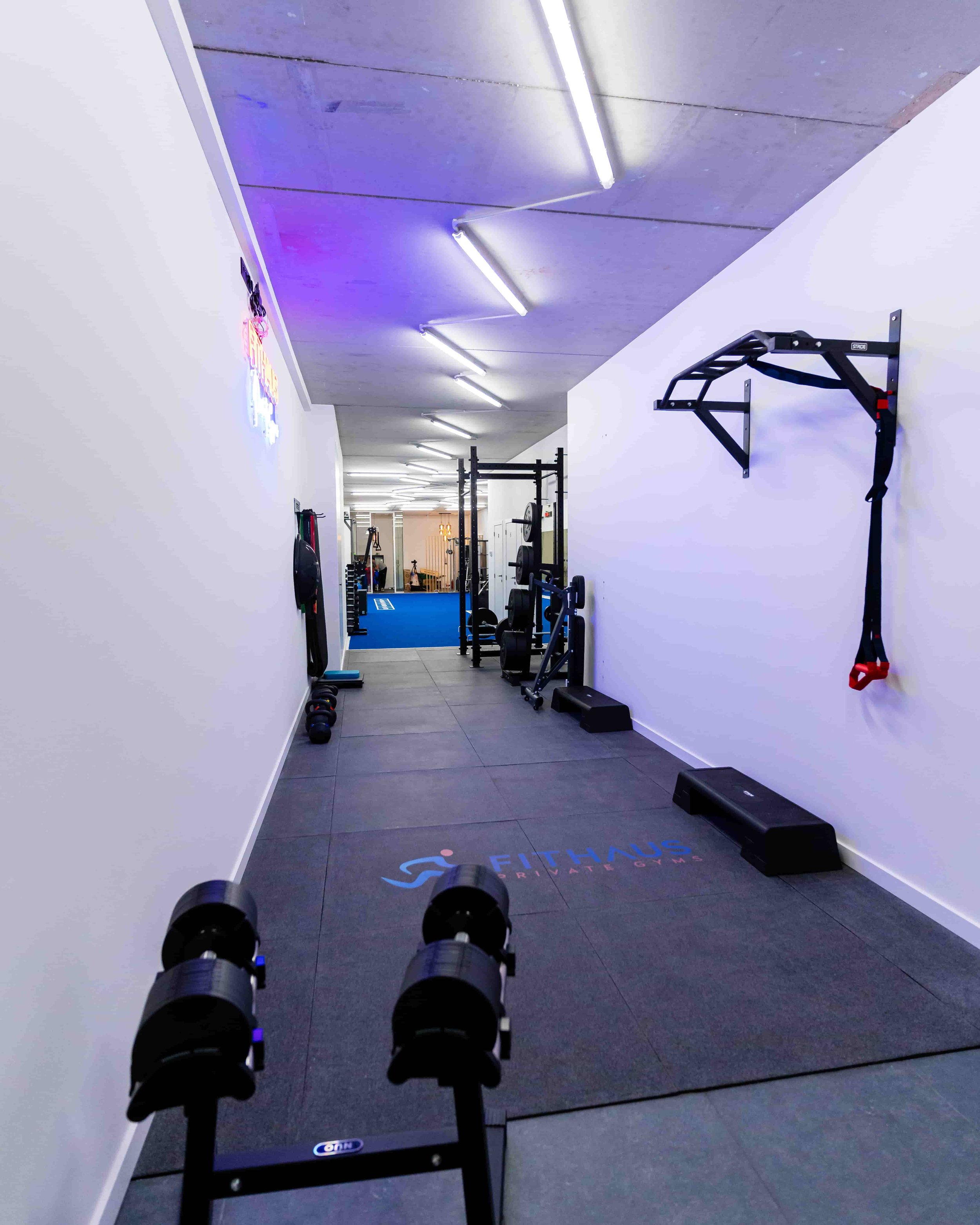 Binnenruimte van een sportschool met fitnessapparatuur en gewichten, witte muren en een plafond met neonlichten