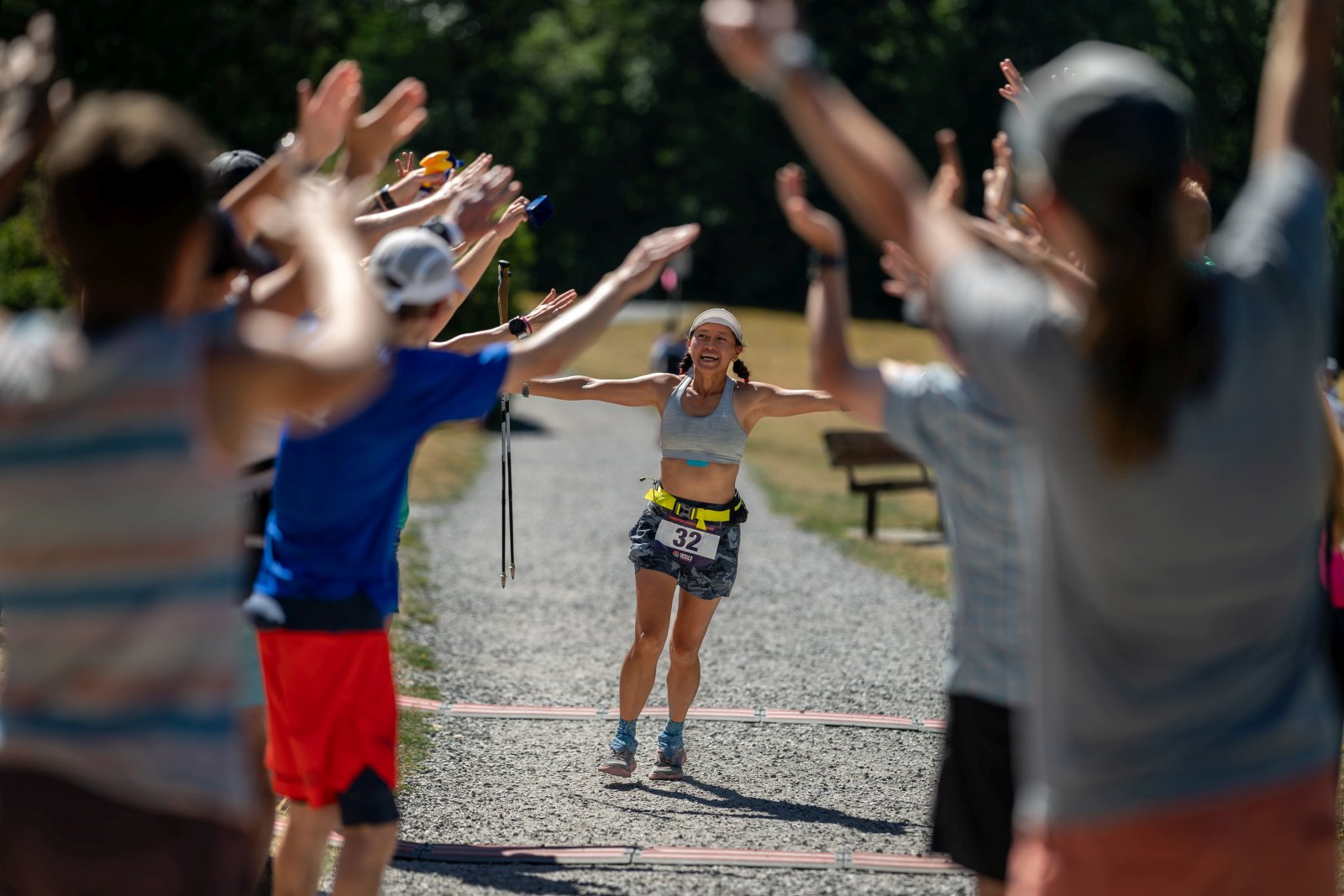 A woman finishing a race, running on a gravel path and high-fiving a crowd of spectators and supporters.