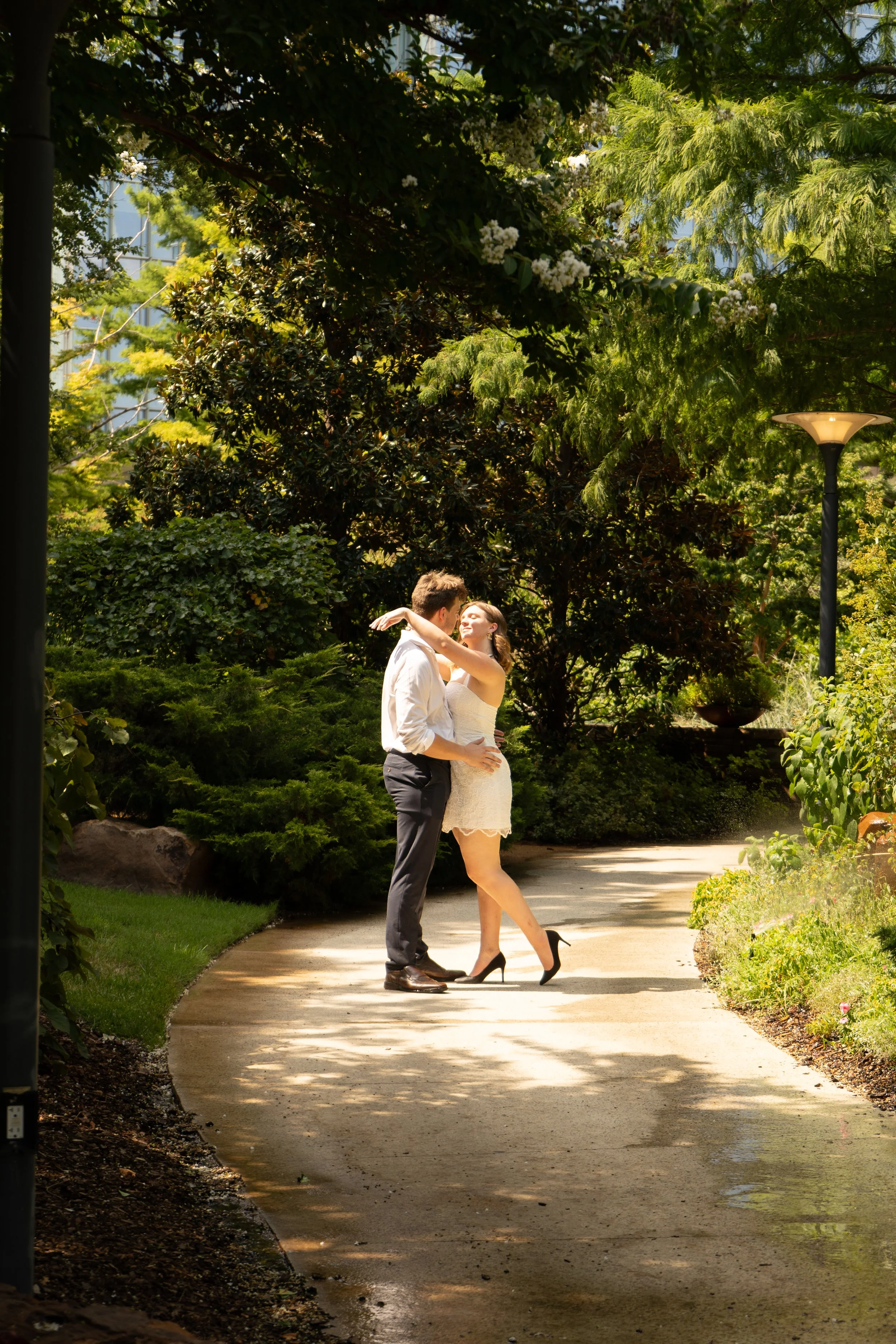 A couple dancing in a park surrounded by lush greenery on a sunny day.
