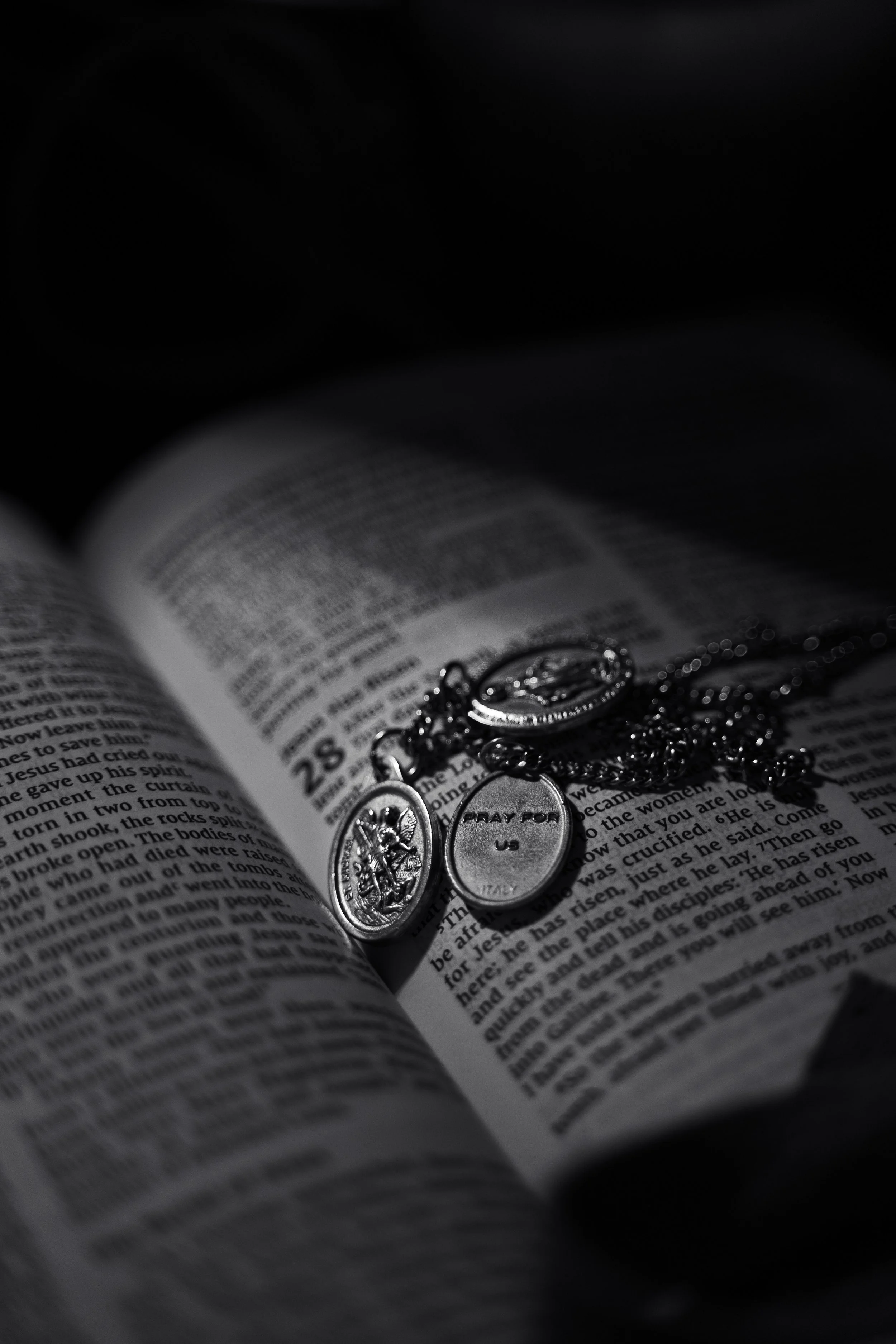 Open Bible with silver necklaces and pendants resting on its pages, with text from a religious passage visible.