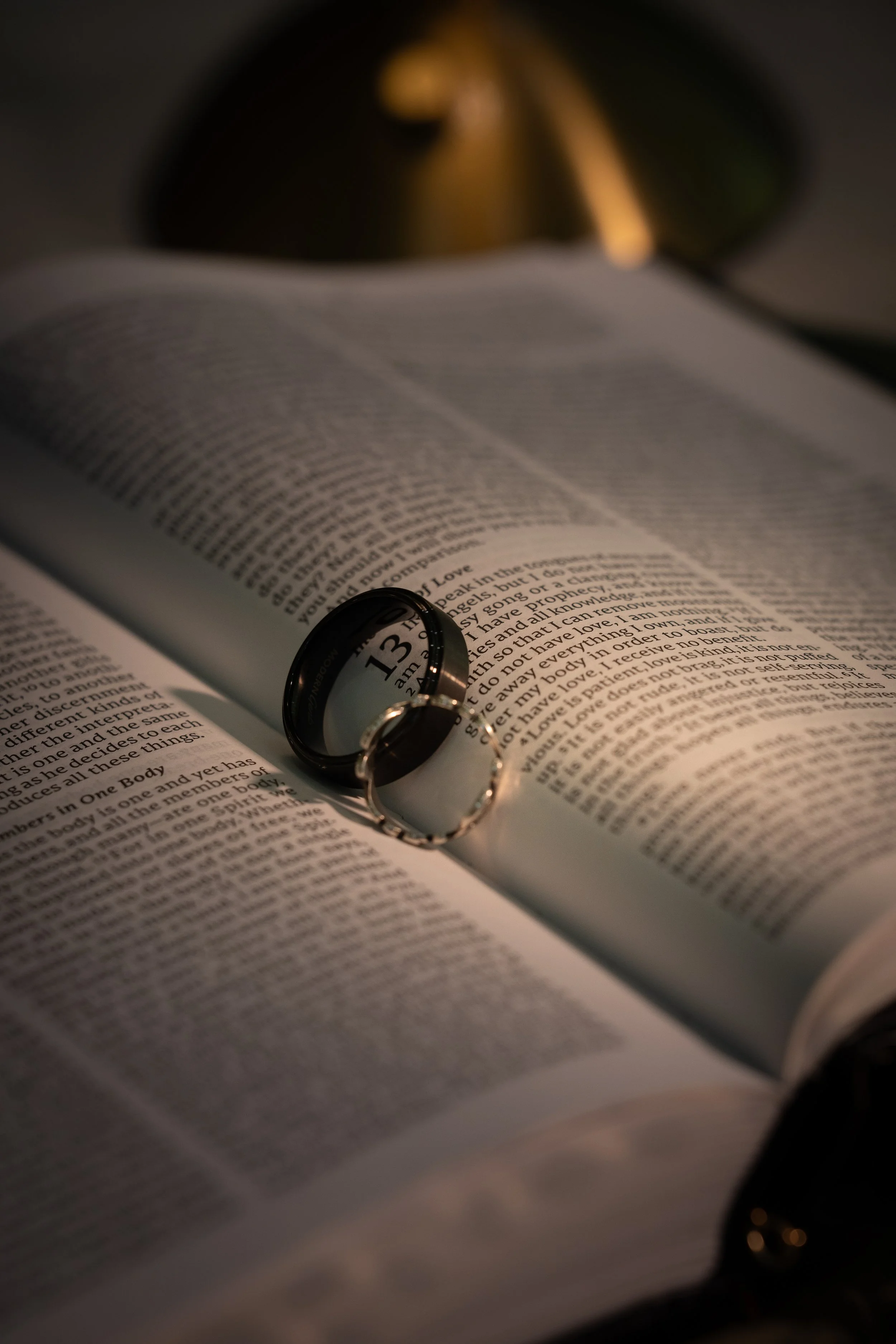 An open book with a ring magnifying a verse of text, and a blurred lamp in the background.