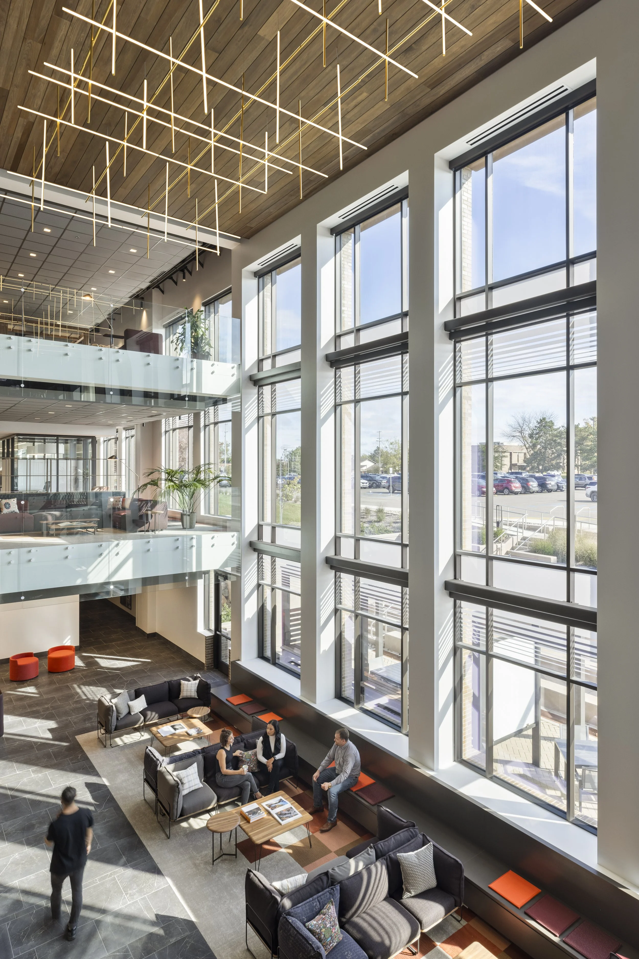 Interior of a modern multi-story building with large windows, seating area, and people socializing.