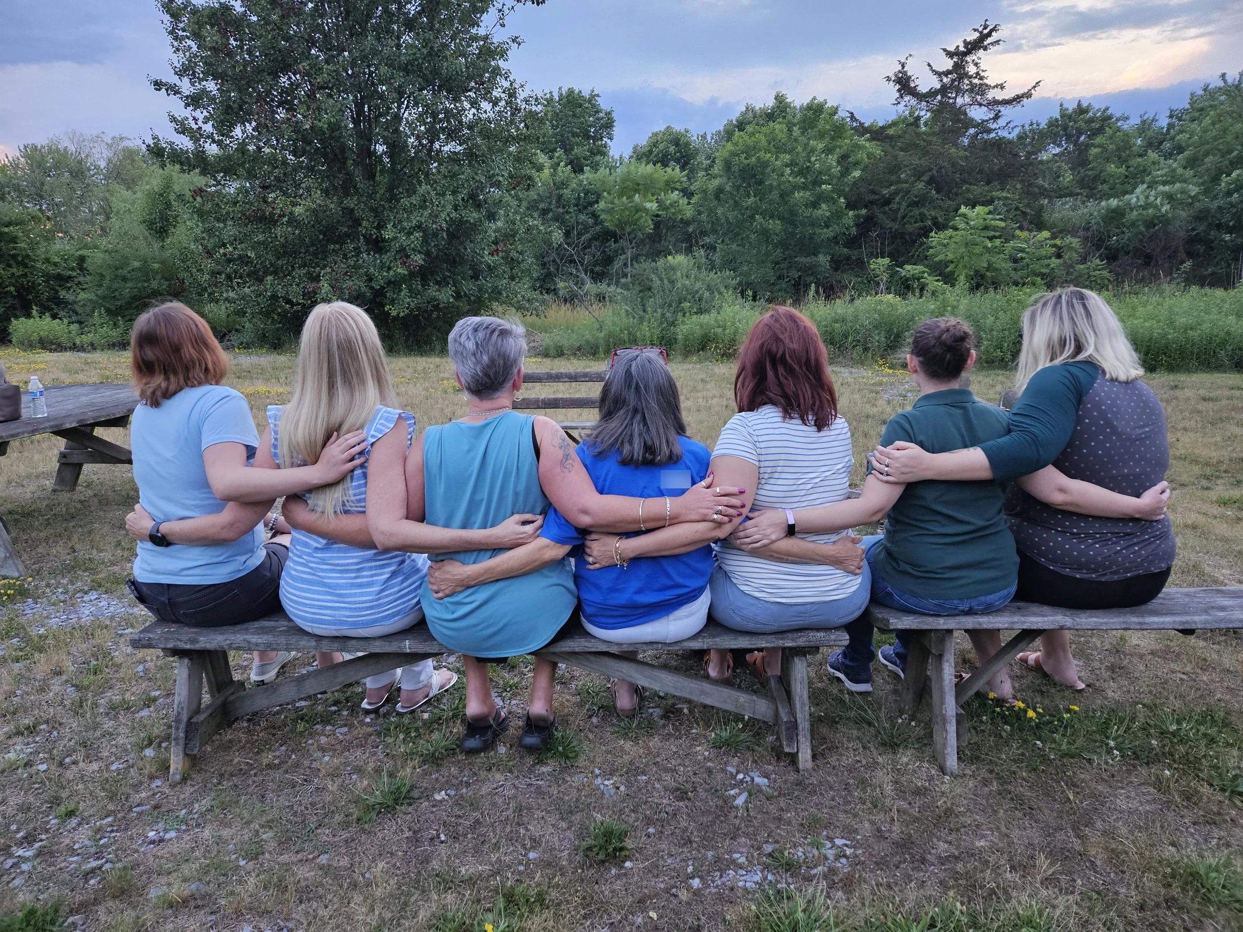 Group of women sitting on a wooden bench outdoors embracing.