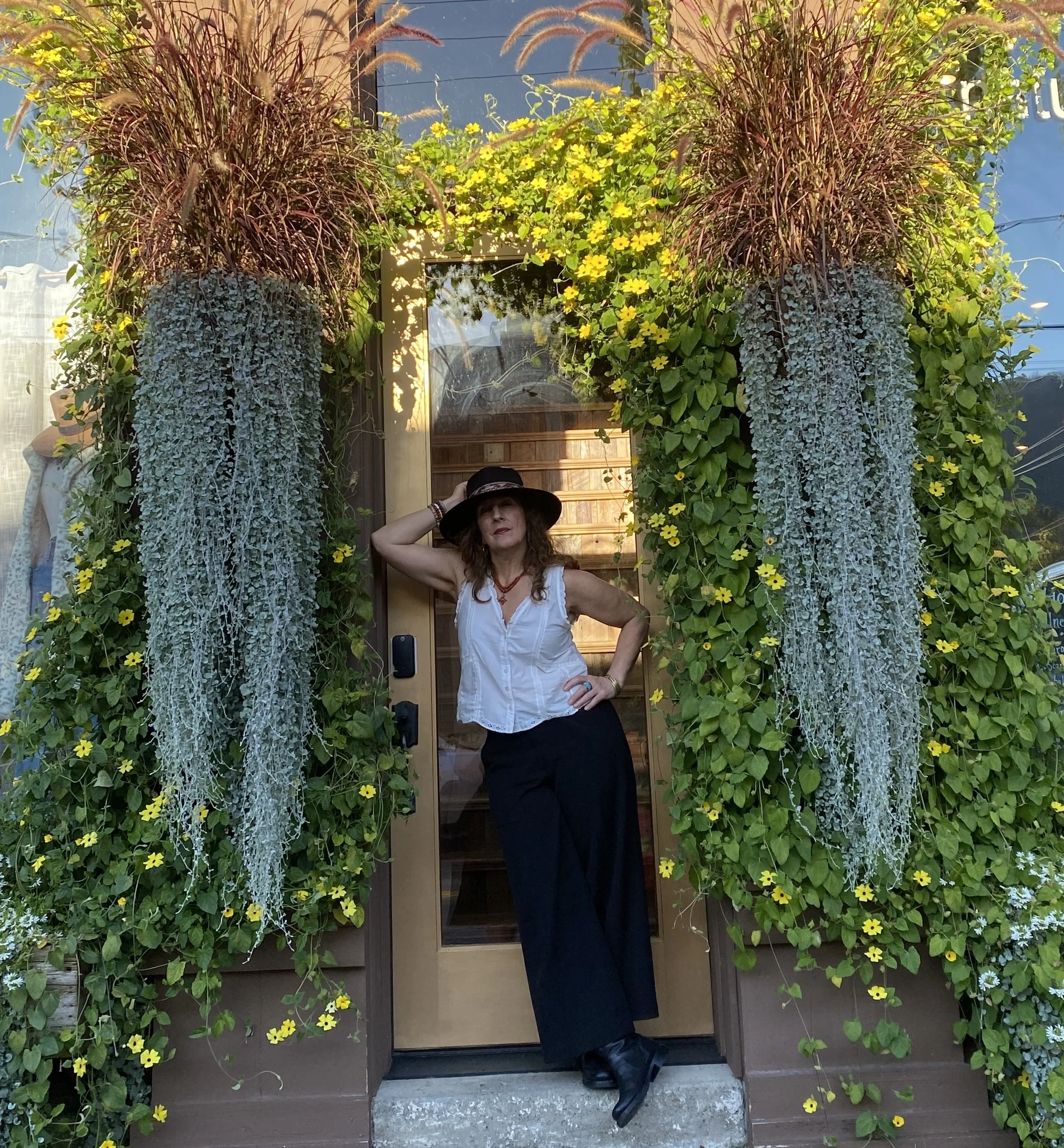 Suzanne Roberts standing in a doorway framed by hanging plants and flowers